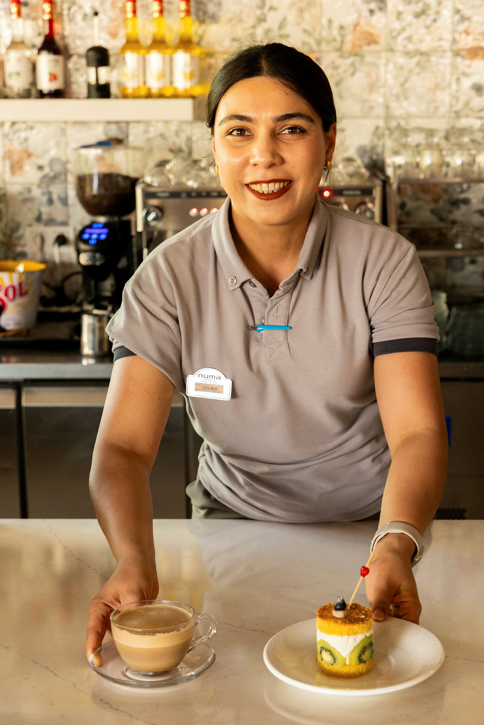 En person kledd i uniform holder en kopp kaffe og en tallerken med en dessert bakverk på en disk. (AI-generert tekst)