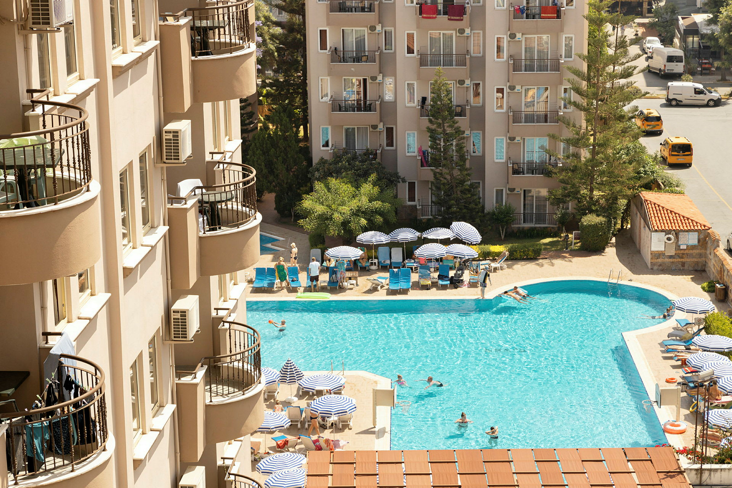 Et hotellbasseng med solsenger og parasoller i nærheten av bygninger. (AI-generert tekst)