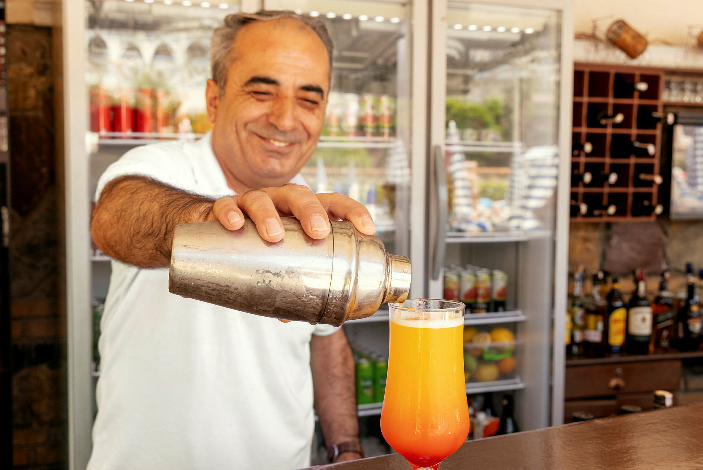 En person holder en cocktailshaker og heller en drikke i et glass. (AI-generert tekst)