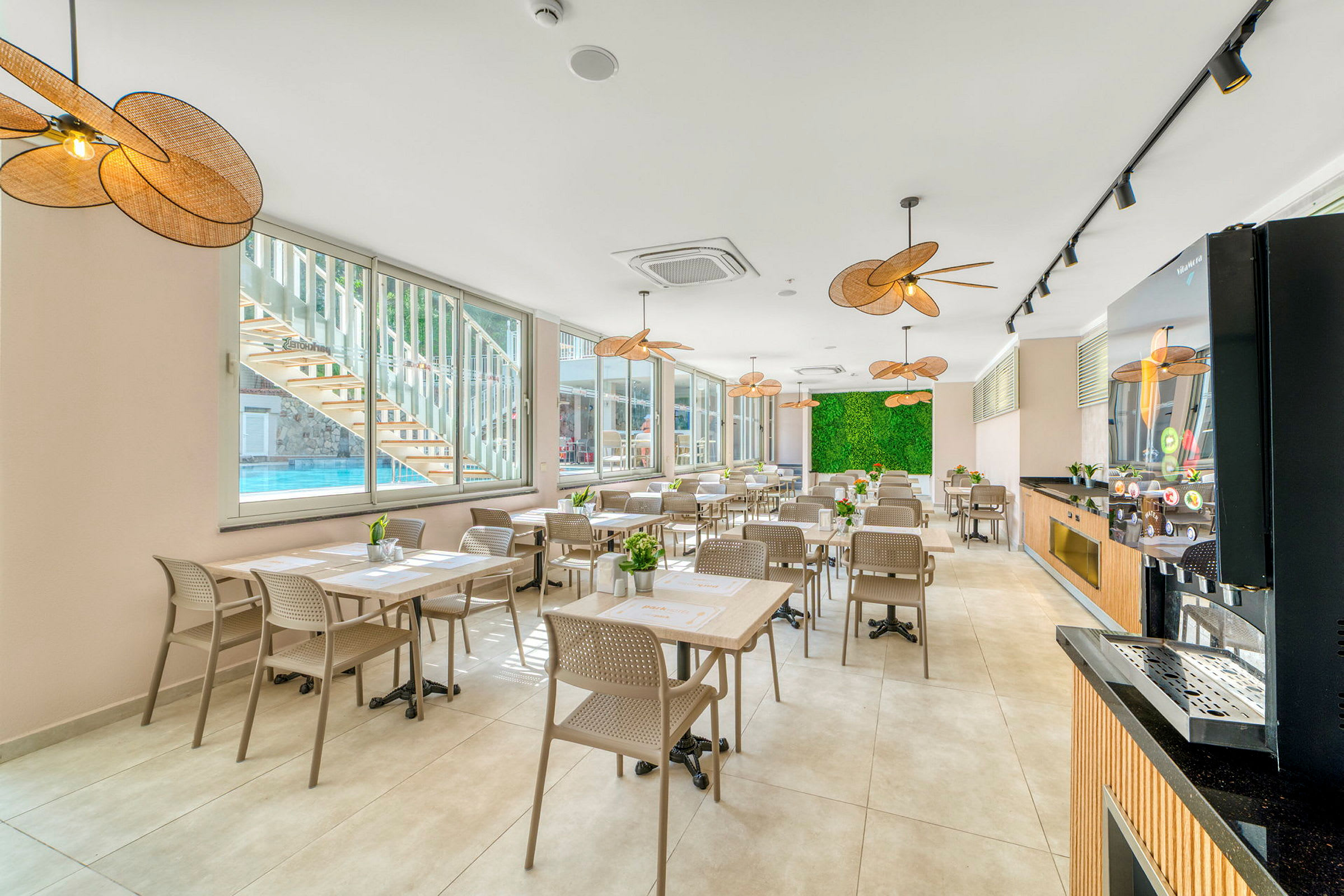 Restaurant med bord og stoler, store vinduer og grønn dekorativ vegg. (AI-generert tekst)