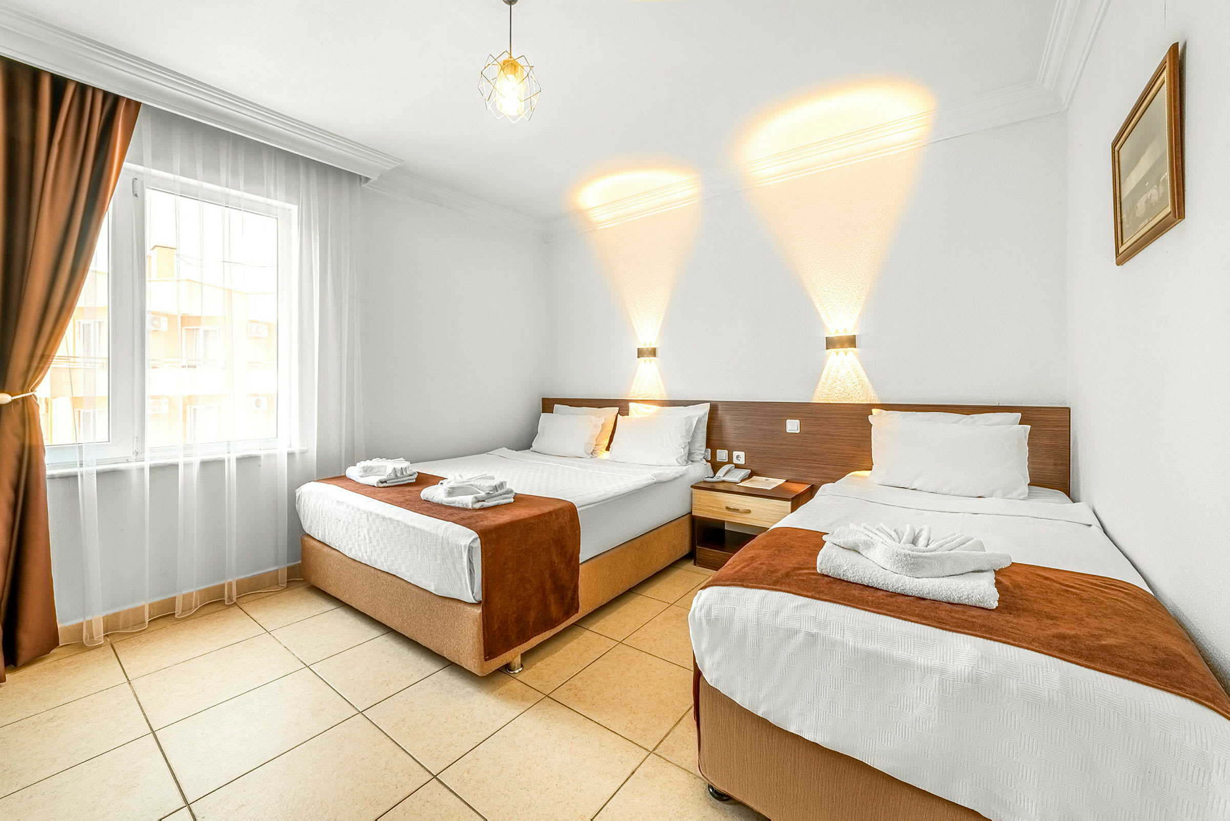 Hotellrom med to separate senger, lys innredning og et vindu med mørke gardiner. (AI-generert tekst)