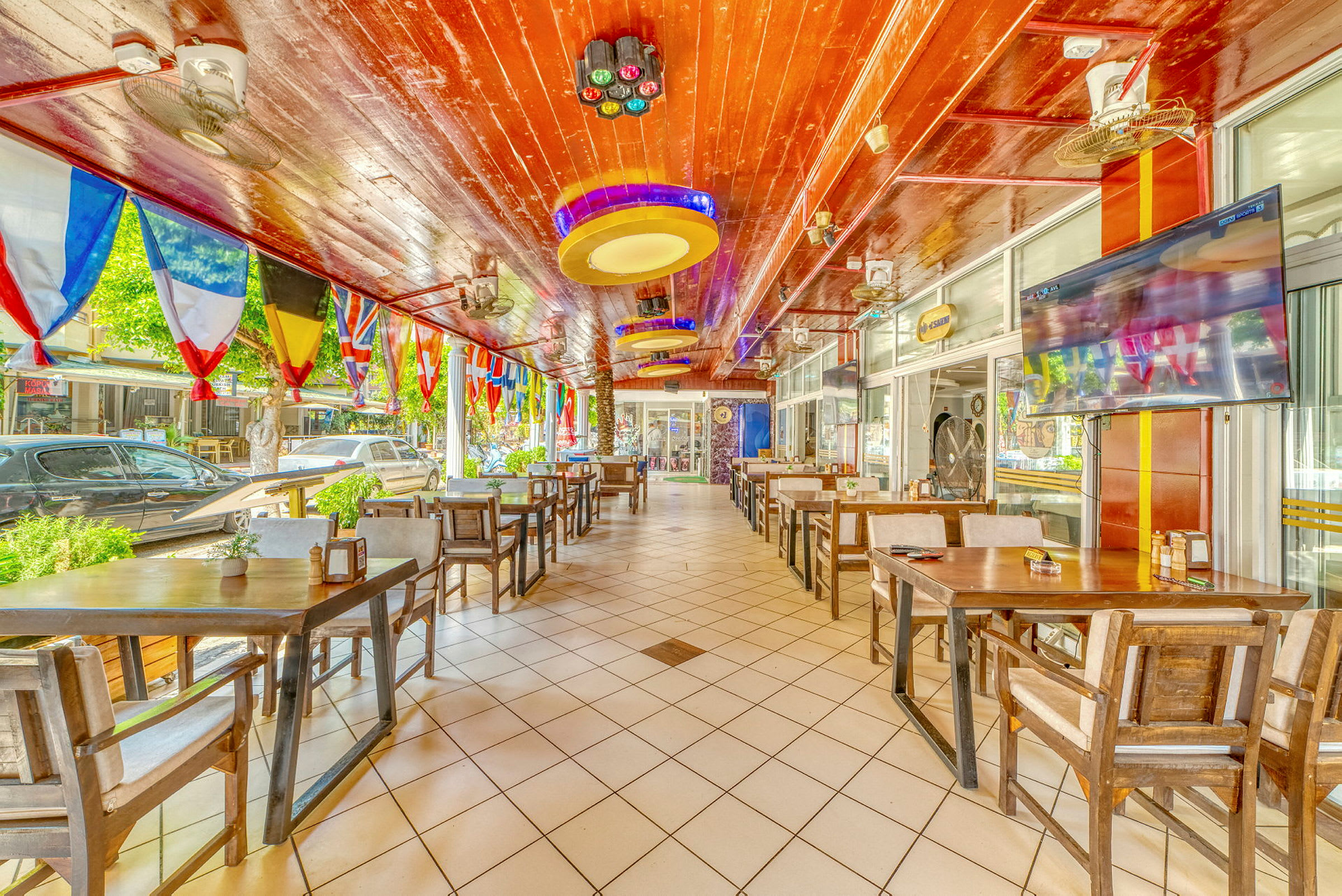 Restaurant med trebord og stoler samt fargerike flagg hengende fra taket. (AI-generert tekst)