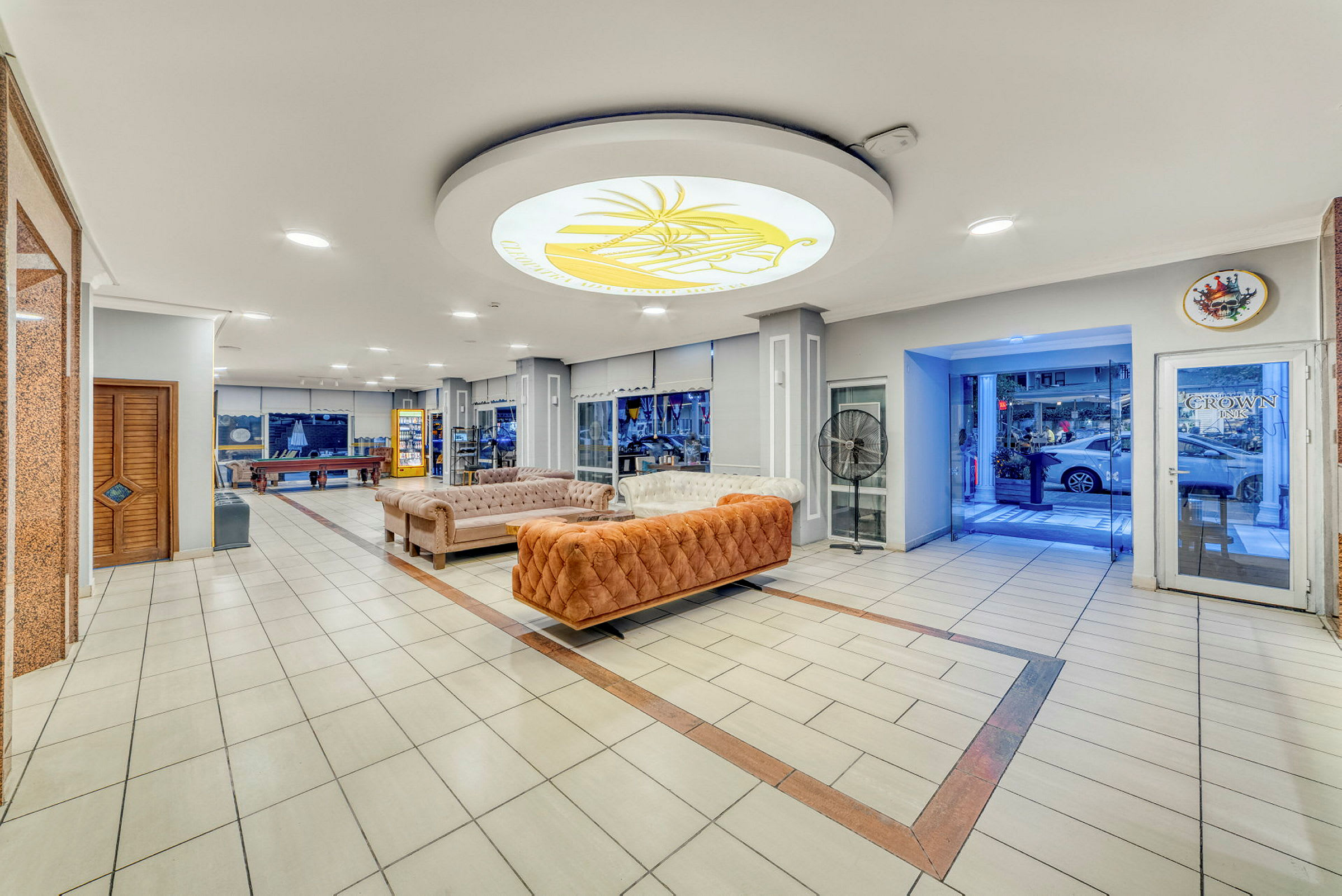 Hotellobby med sofaer, bordspill og en glassinngang. (AI-generert tekst)