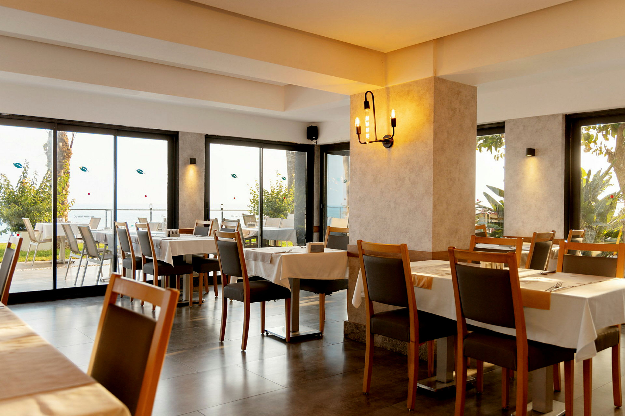Restaurantinteriør med bord og stoler samt utsikt mot natur og lysinnfall. (AI-generert tekst)