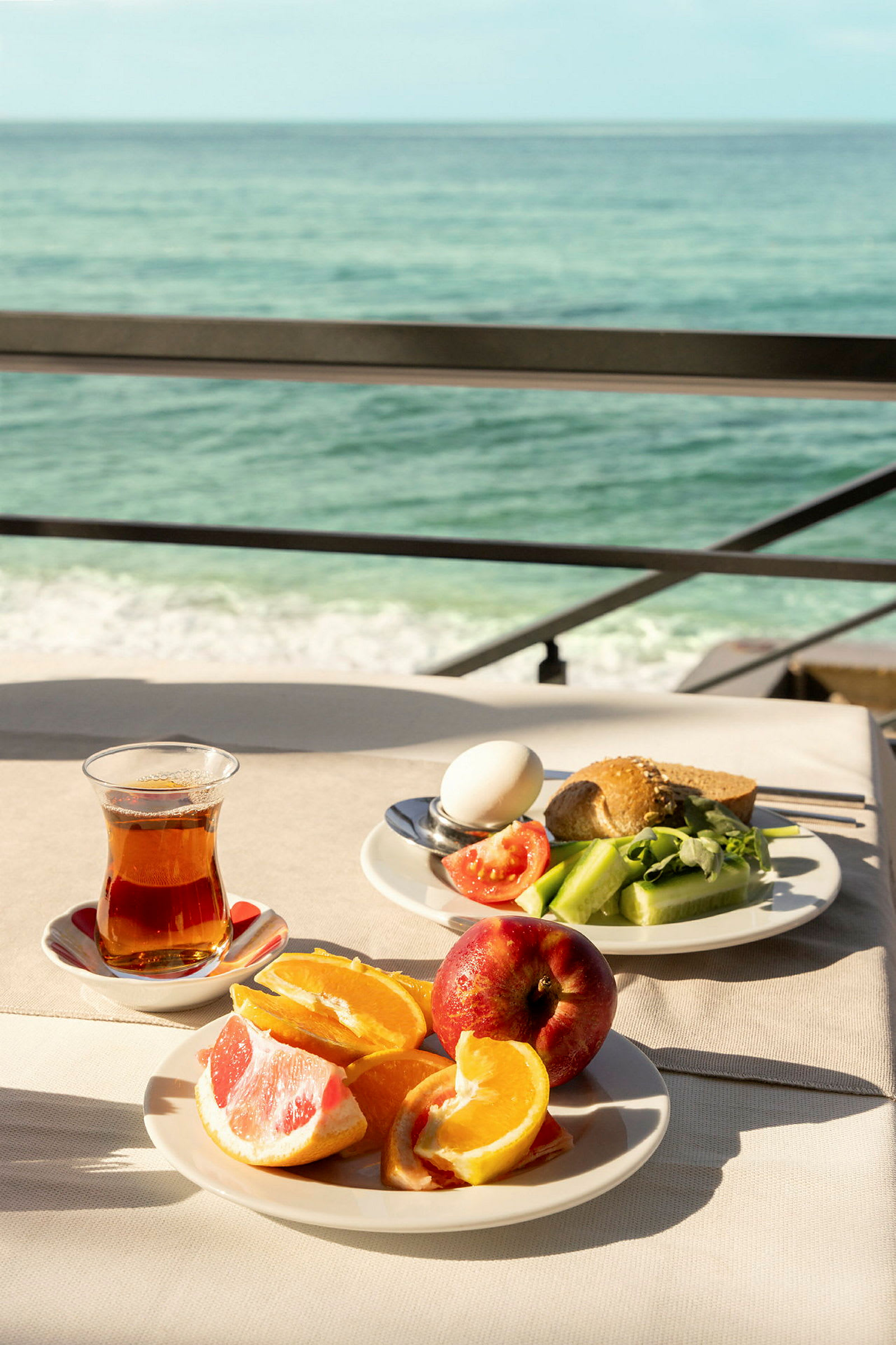 Frokost med havutsikt, inkludert appelsinbåter, grapefrukt, eple, te og salat. (AI-generert tekst)