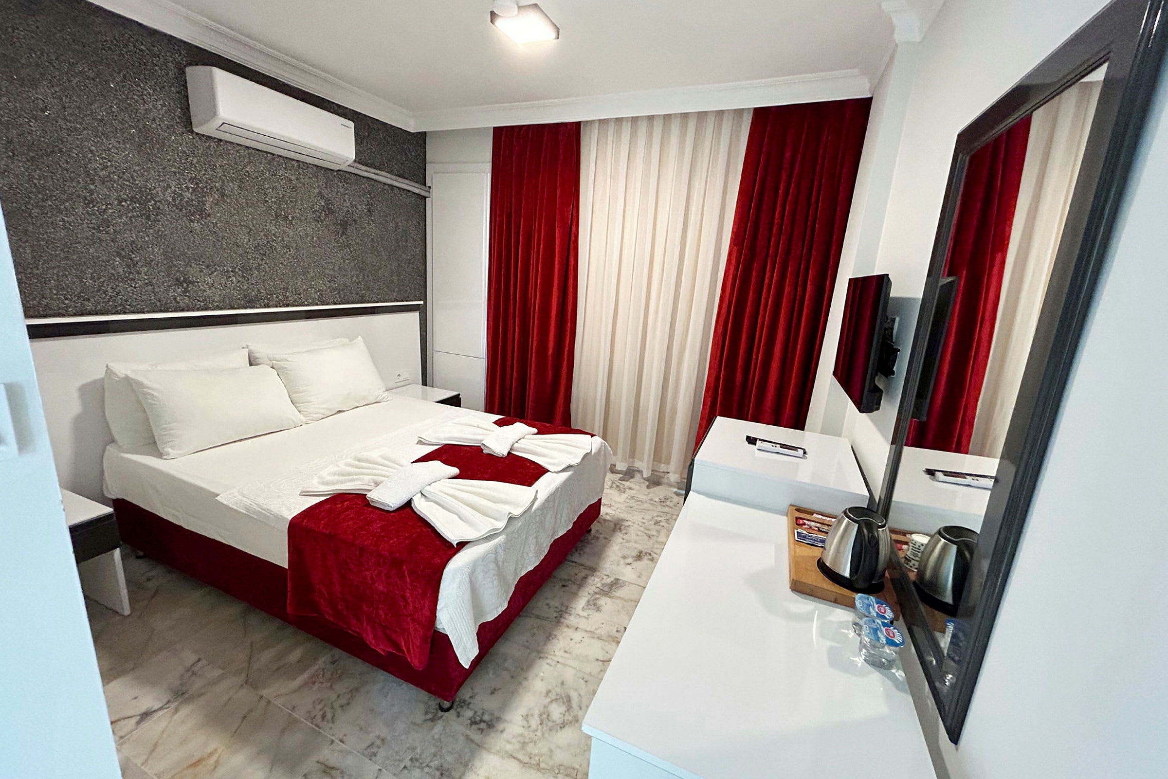 Et hotellrom med en dobbeltseng, hvit og rød innredning samt et skrivebord med speil. (AI-generert tekst)