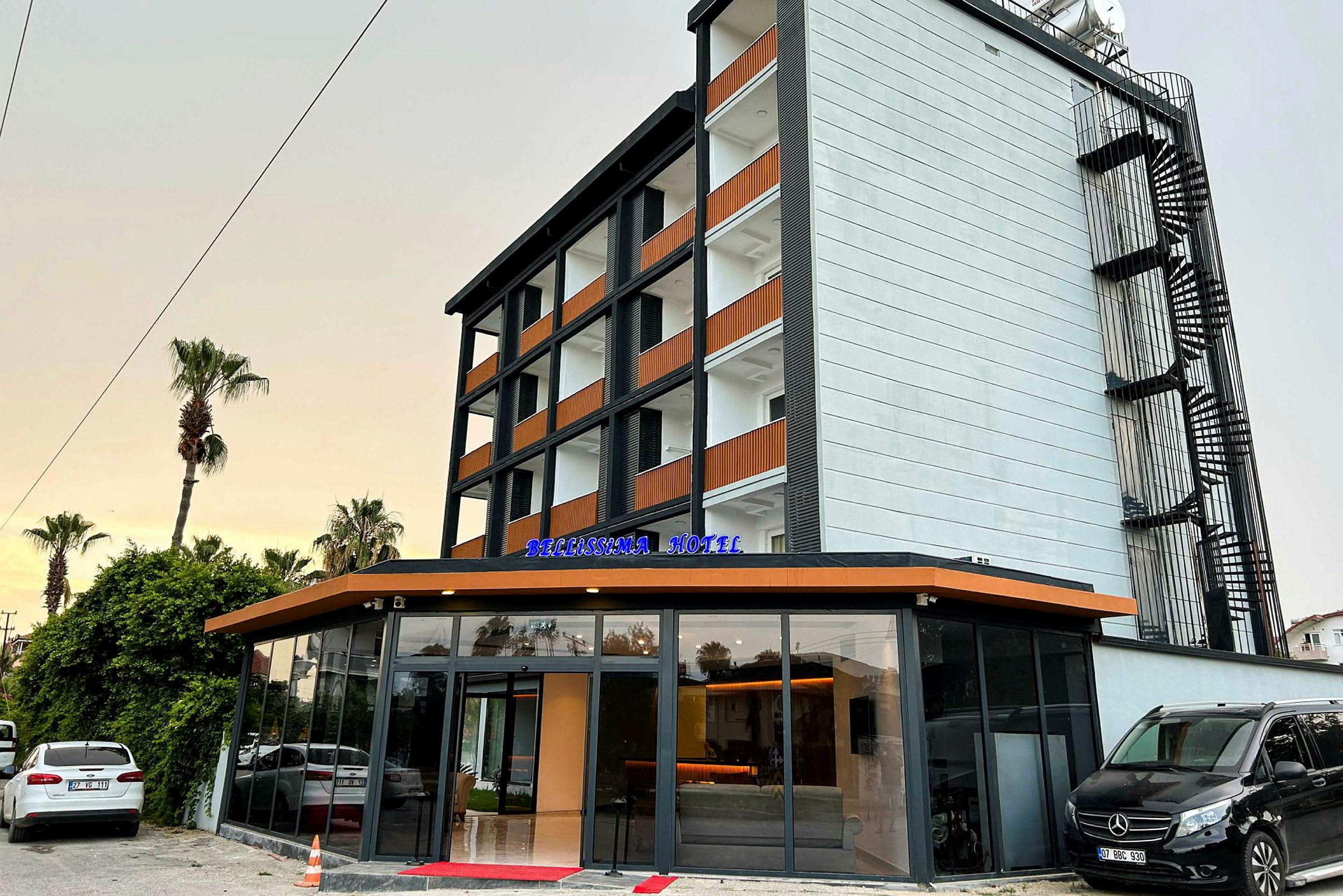 Bygningen er et moderne hotell med fem etasjer og glassinngang. Skilt for "Bellissima Hotel" vises ved inngangen. (AI-generert tekst)
