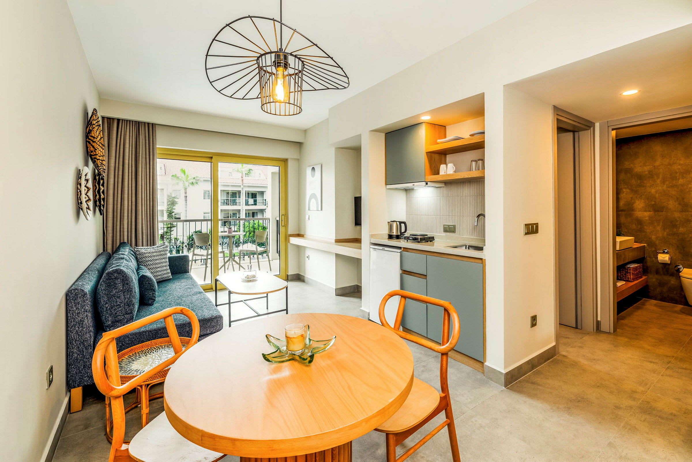 Et moderne hotellrom med sittegruppe, spisebord, kjøkkenområde og et bad i bakgrunnen. (AI-generert tekst)