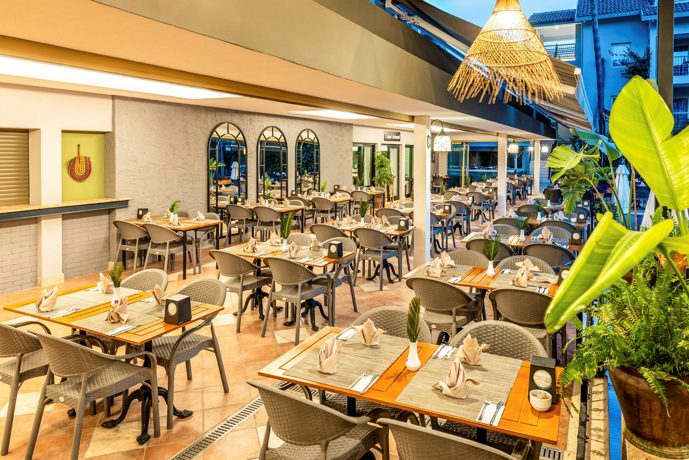 Et restaurantmiljø med bord og stoler klare, dekorert med planter og pent plasserte servietter. (AI-generert tekst)