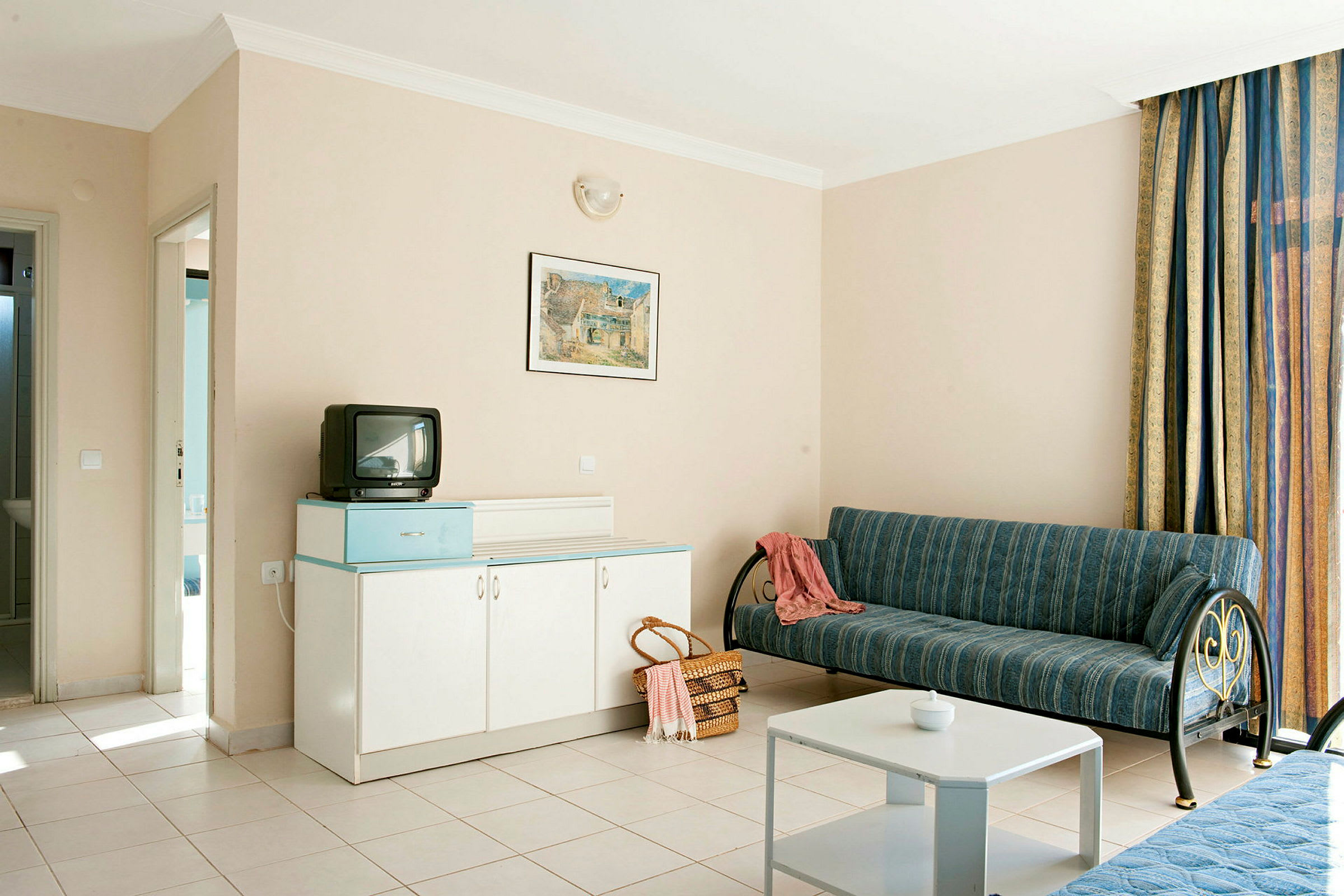 Hotellrom med sofa, bord, skap og liten TV. (AI-generert tekst)