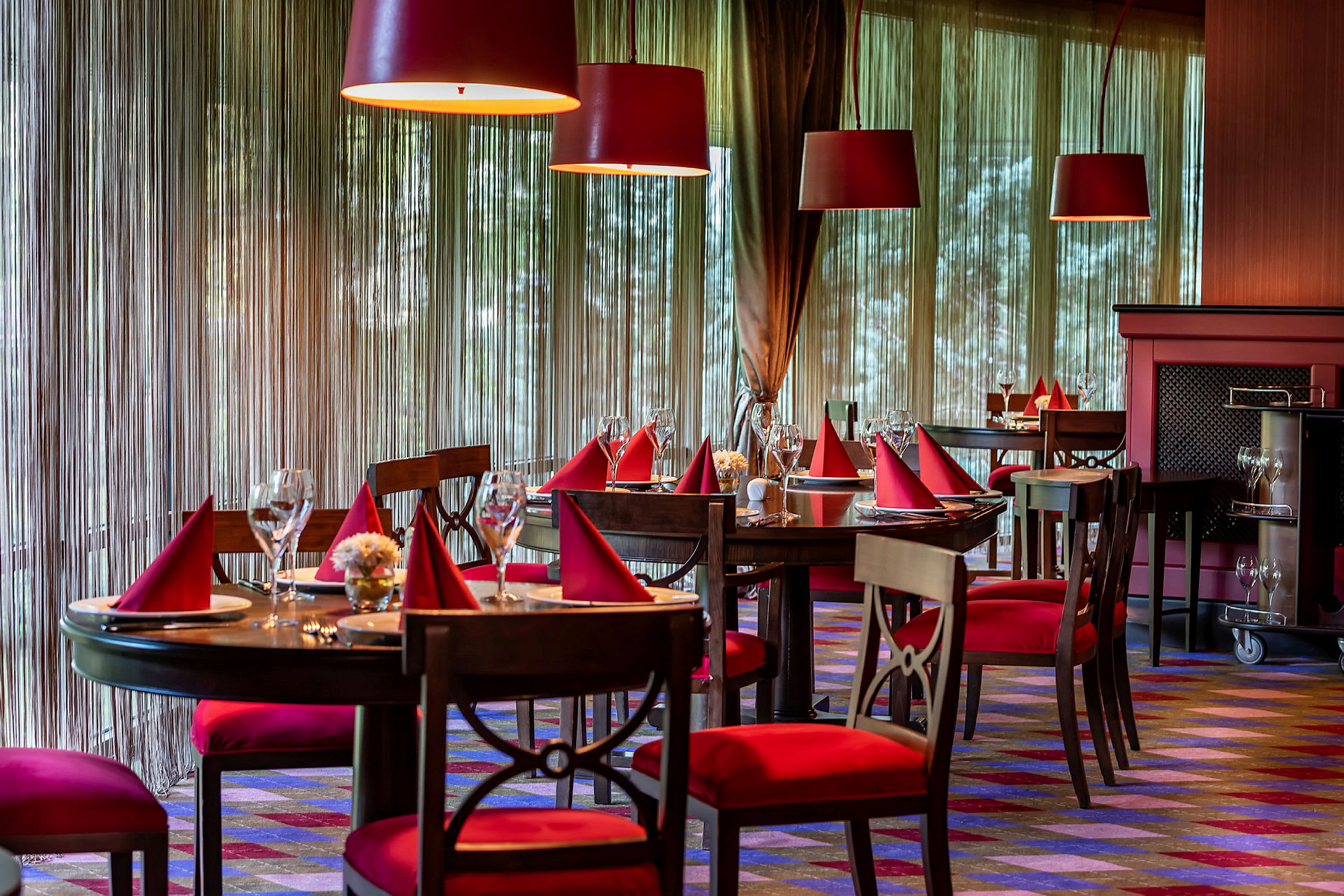 En elegant restaurant med bord dekket med røde servietter og glass. (AI-generert tekst)