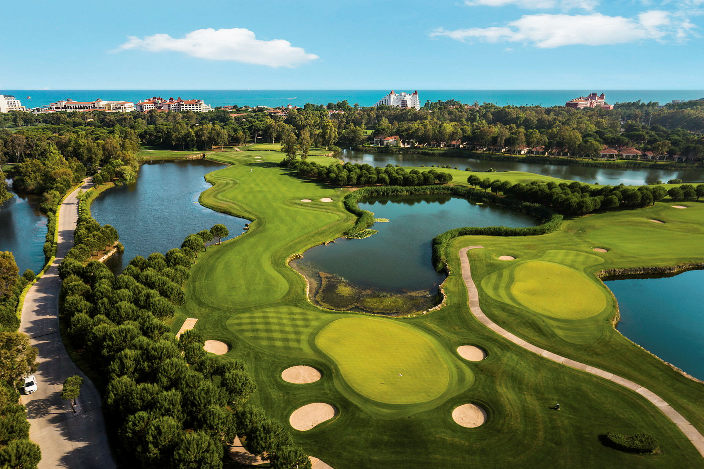 Flyfoto av en golfbane med grønne fairways, bunkere og vannhindringer, omgitt av hoteller og trær. (AI-generert tekst)