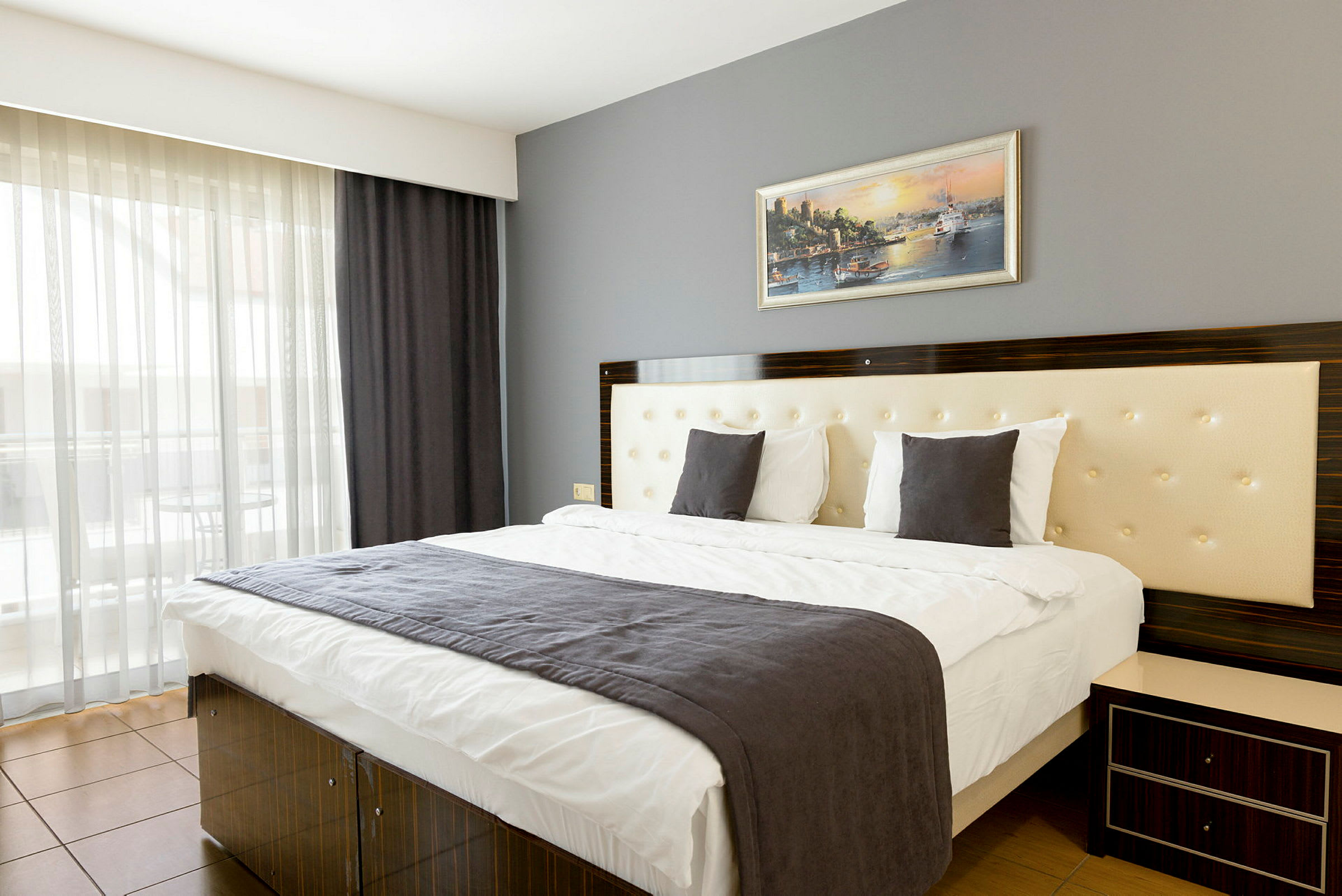Et moderne hotellrom med en dobbeltseng, en grå sengepute og et maleri på veggen. (AI-generert tekst)