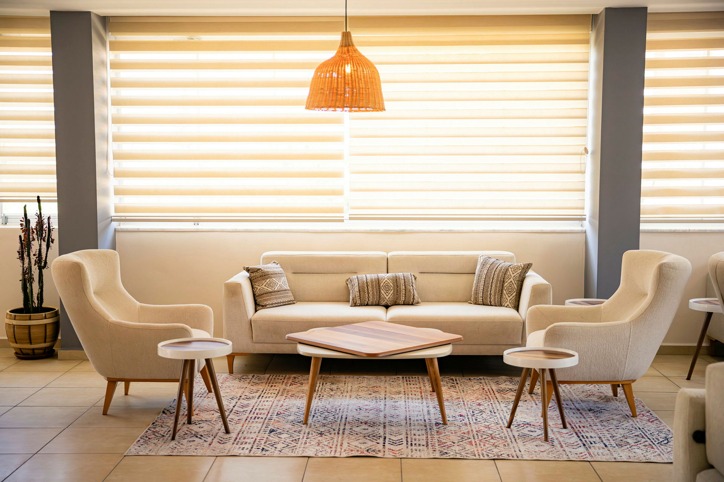 En lys og stilren sittegruppe med sofa, lenestoler og småbord. Lysinnslipp fra vinduer med persienner. (AI-generert tekst)