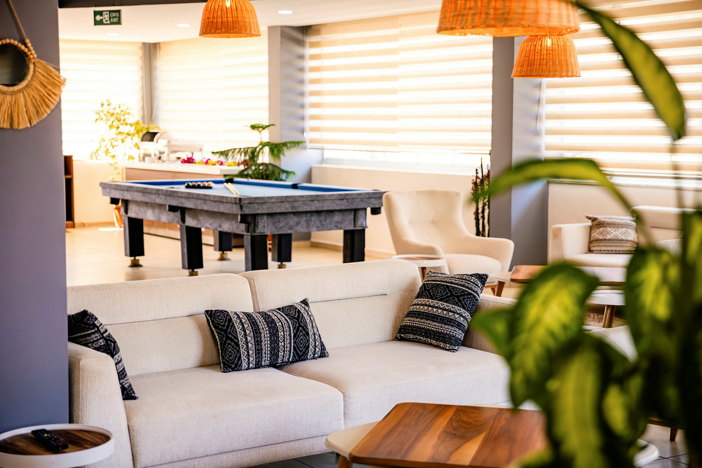 En lys og elegant lounge med sofaer, puter og et biljardbord i bakgrunnen. (AI-generert tekst)