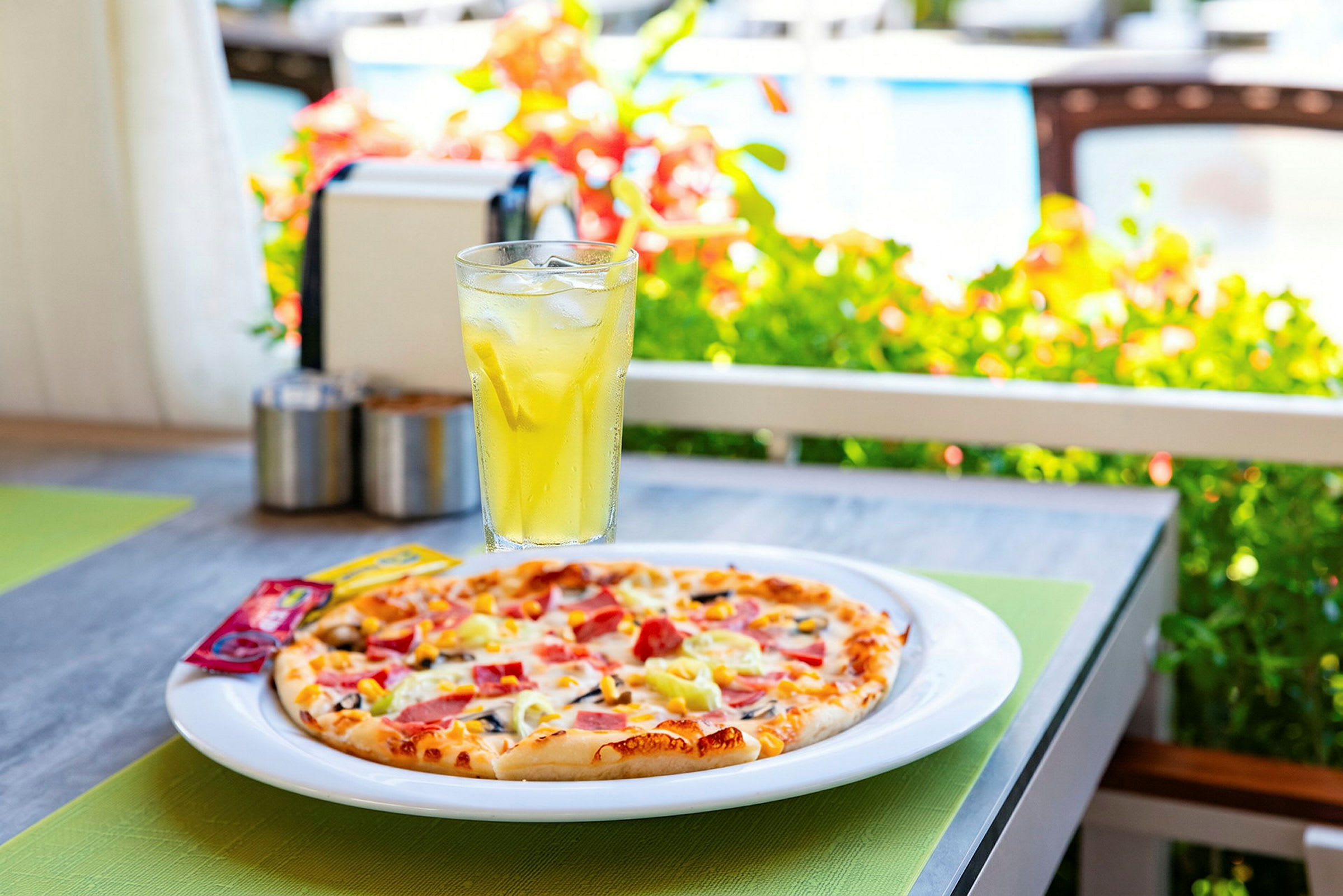 En tallerken med pizza og et glass med gul drikke står på et bord utendørs. (AI-generert tekst)