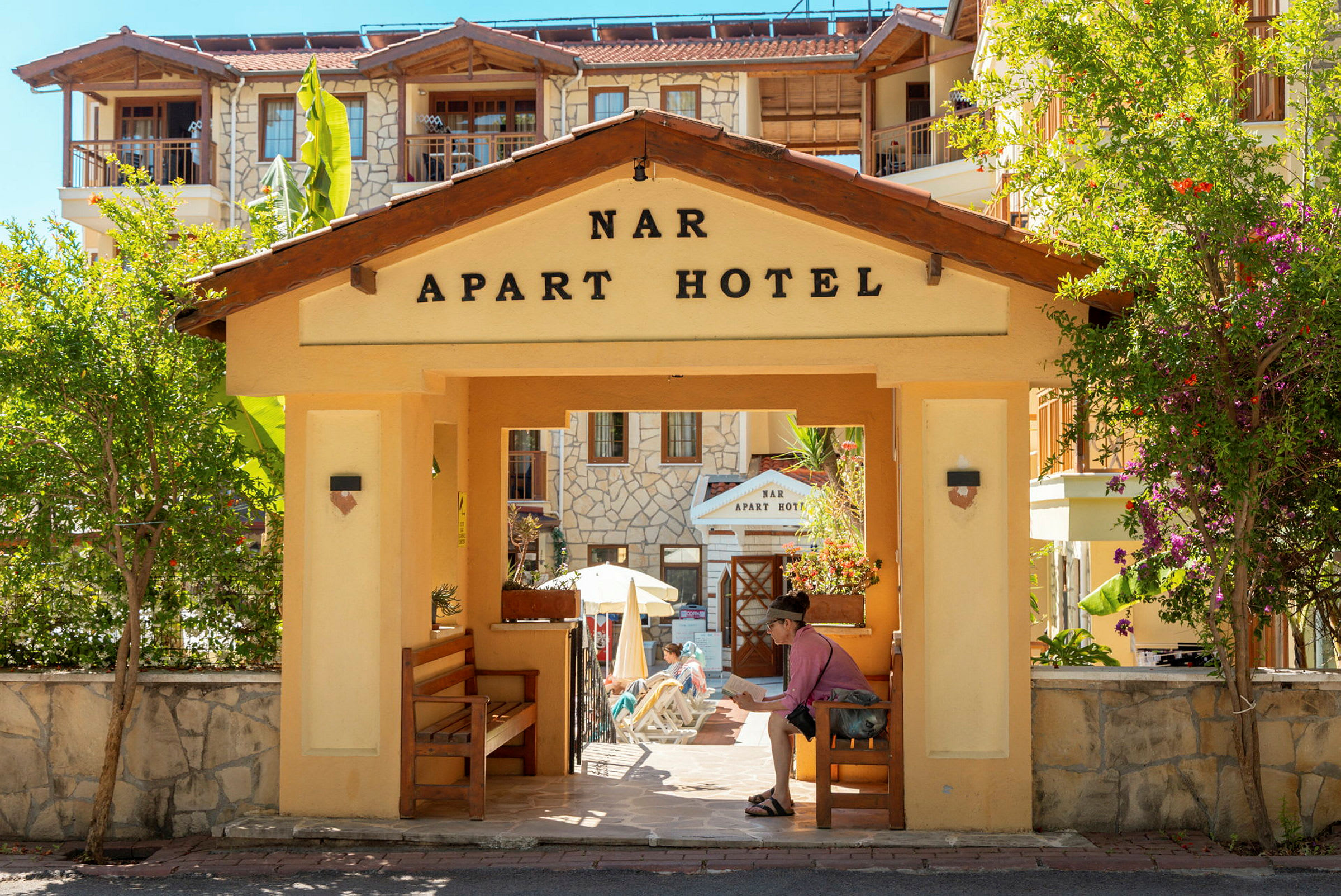 Inngang til Nar Apart Hotel med blomster og vegetasjon. (AI-generert tekst)