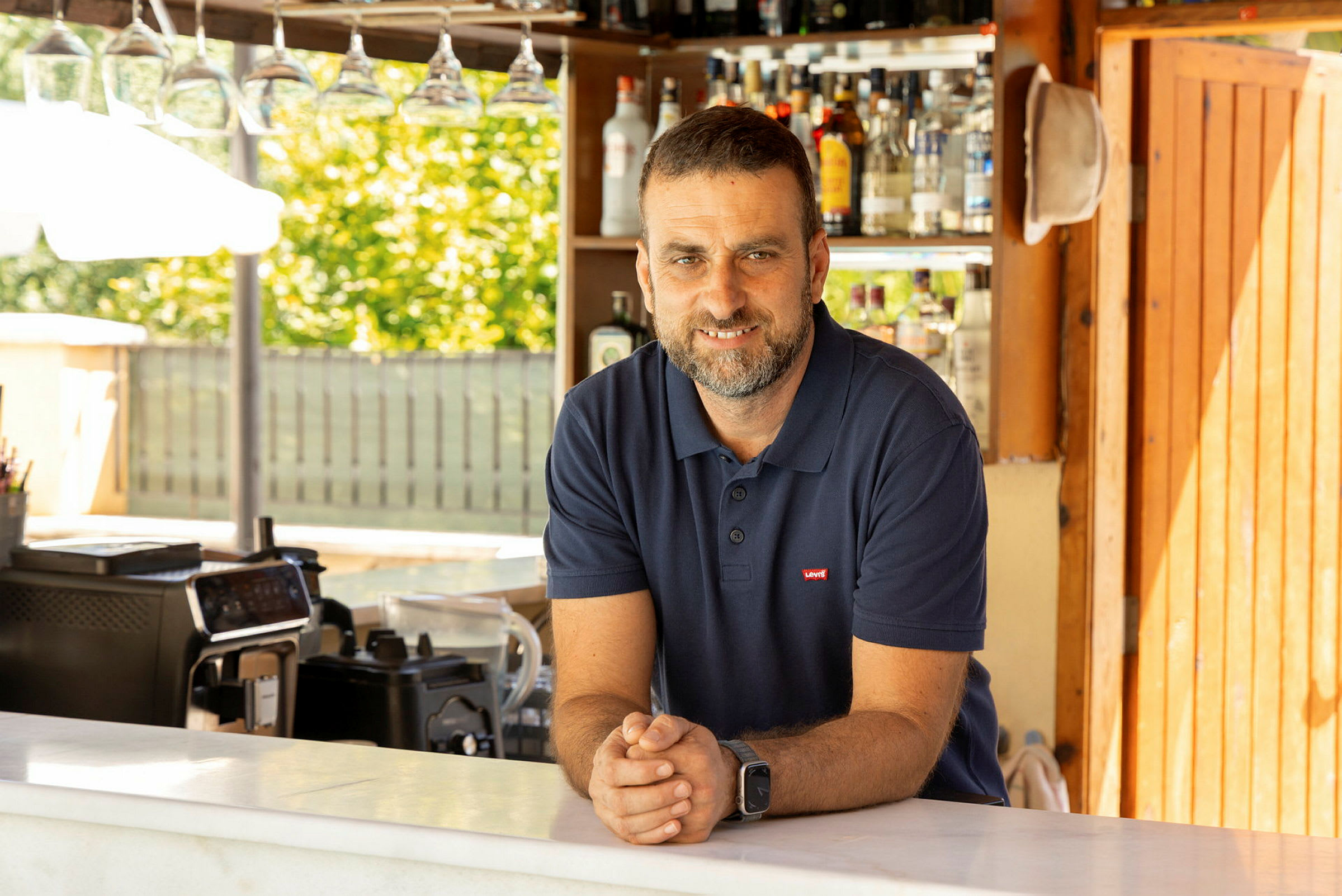 En mann står bak en bar med flasker i bakgrunnen. (AI-generert tekst)