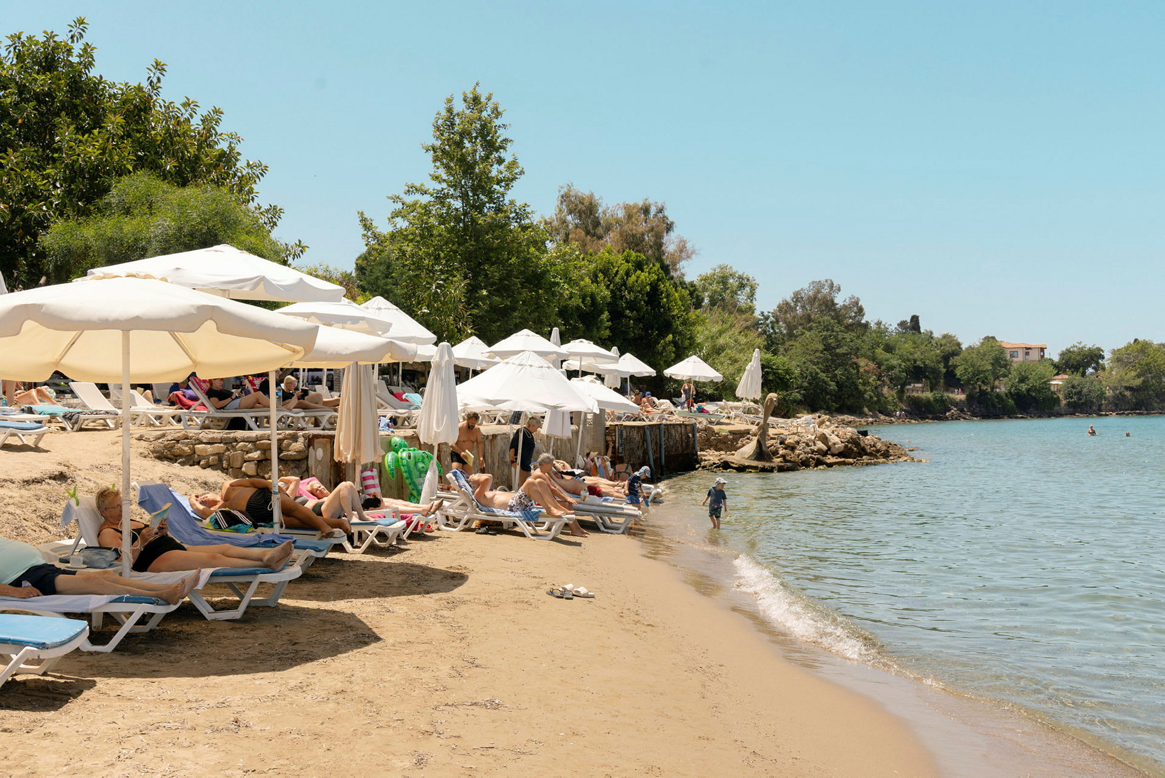 Badestrand med solsenger og parasoller ved en vannkant med klart vann. (AI-generert tekst)