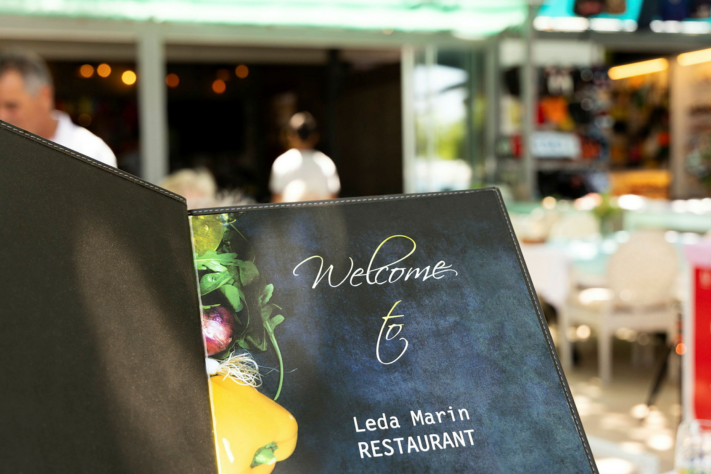 En restaurantmenyforside med teksten 'Welcome to Leda Marin RESTAURANT' og et bilde av grønnsaker på forsiden. (AI-generert tekst)