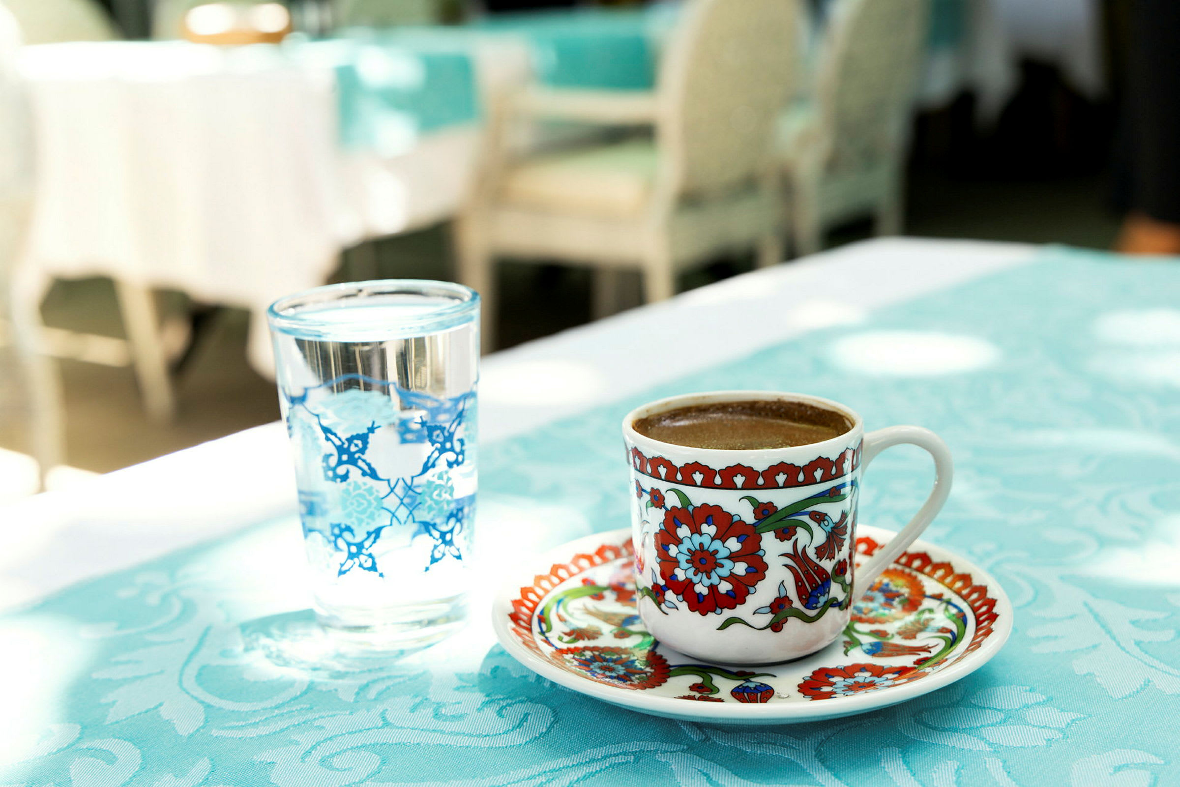 En kopp med fargerikt mønster som inneholder kaffe ved siden av et glass vann på et bord. (AI-generert tekst)