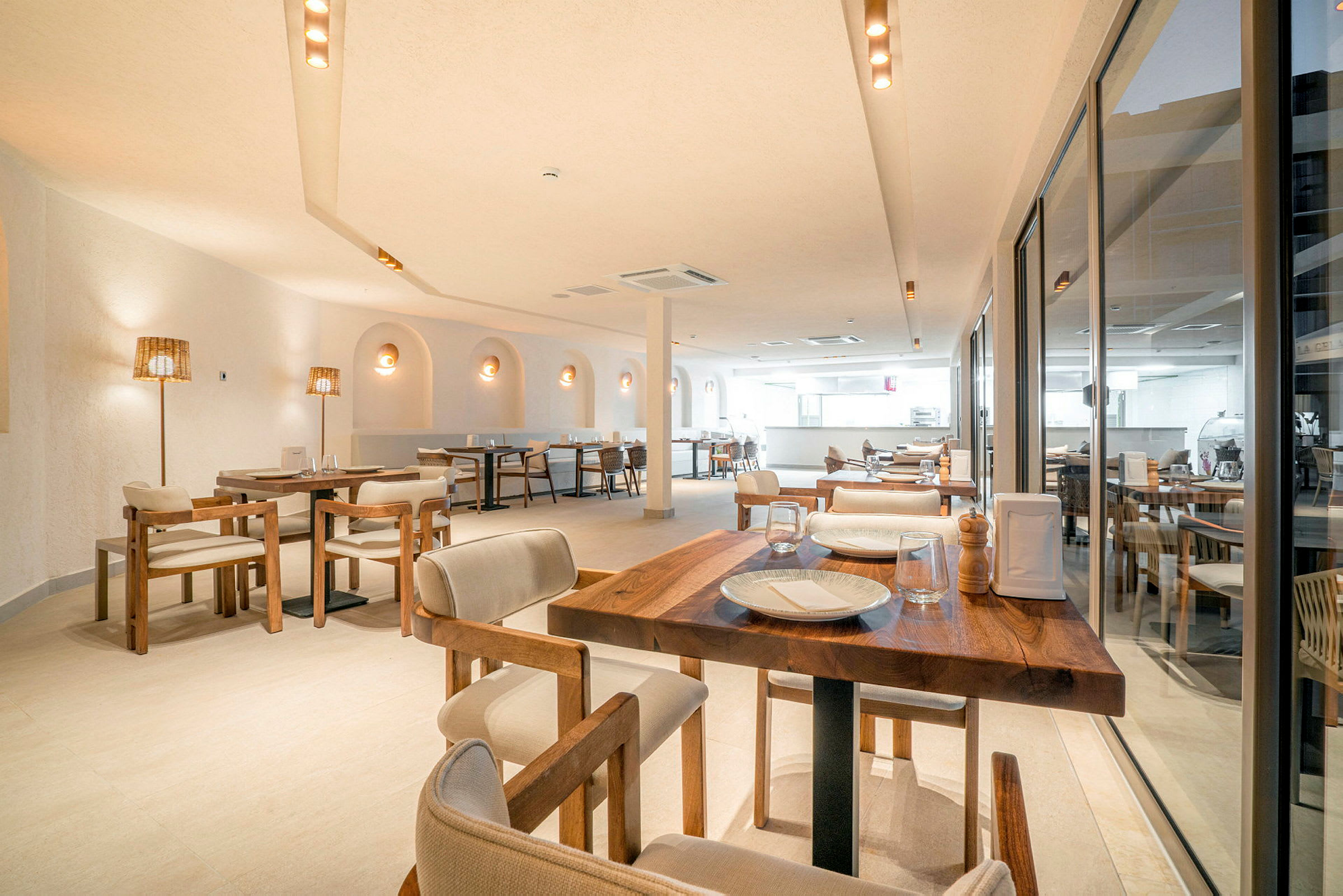 En lys og stilren restaurant med trebord, komfortable stoler og dekorative lamper. Vinduer dekker den ene siden av rommet. (AI-generert tekst)