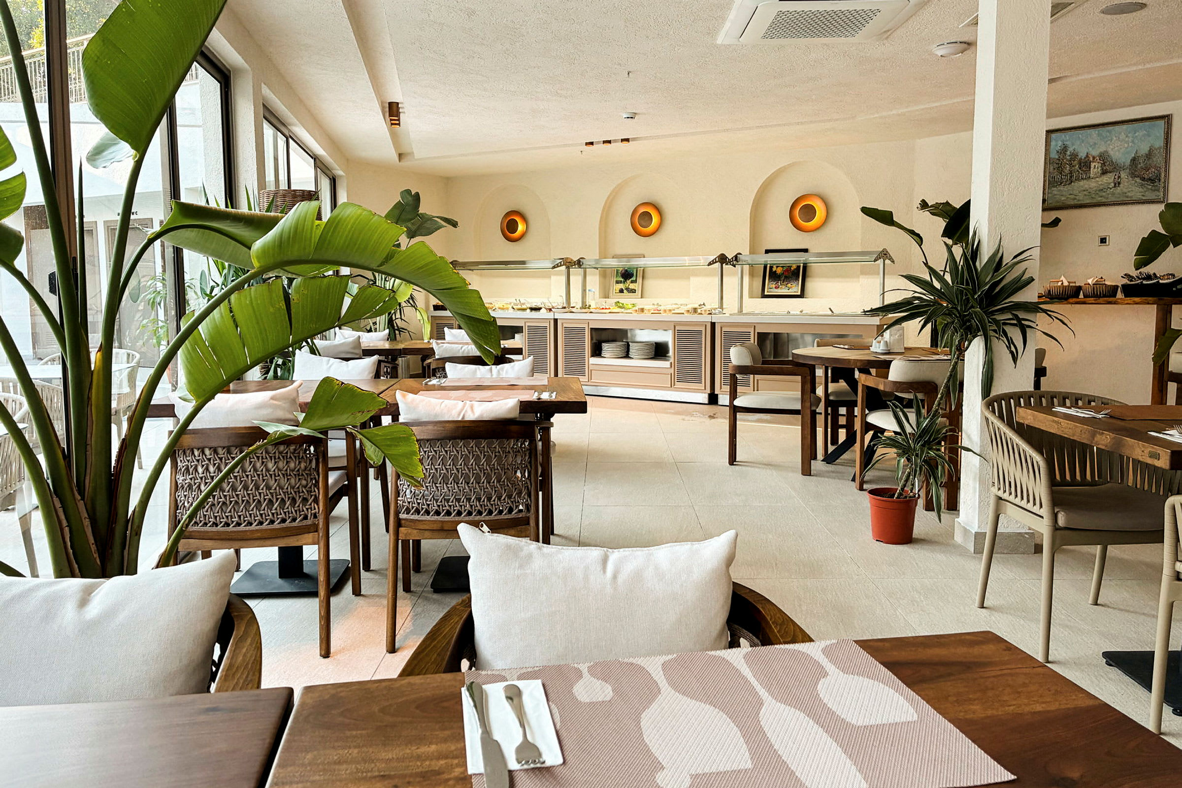 En lys og innbydende restaurant med tremøbler, grøn planteinnredning og et bufféområde i bakgrunnen. (AI-generert tekst)