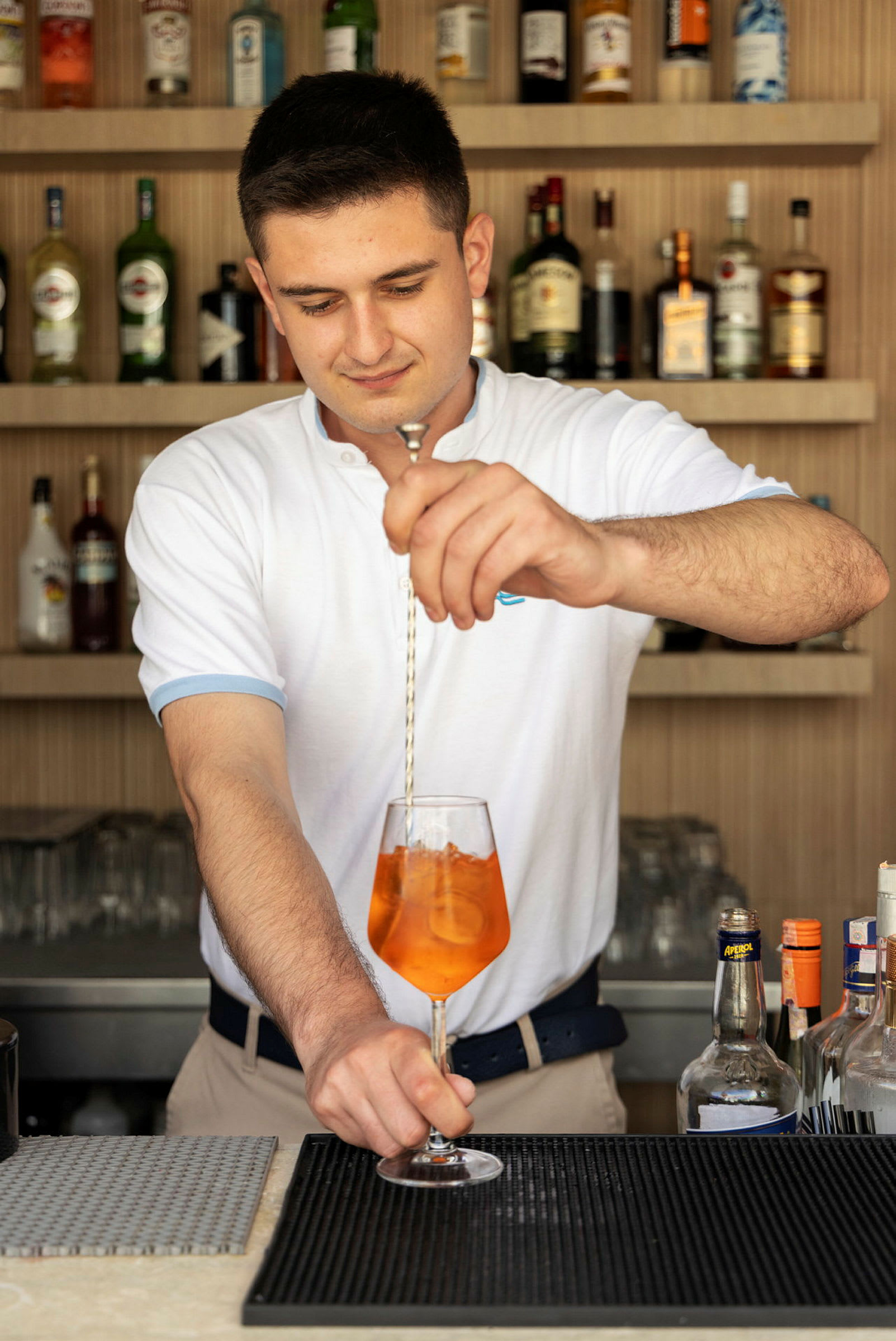 En bartender blander en drink med oransje væske i et vinglass. (AI-generert tekst)