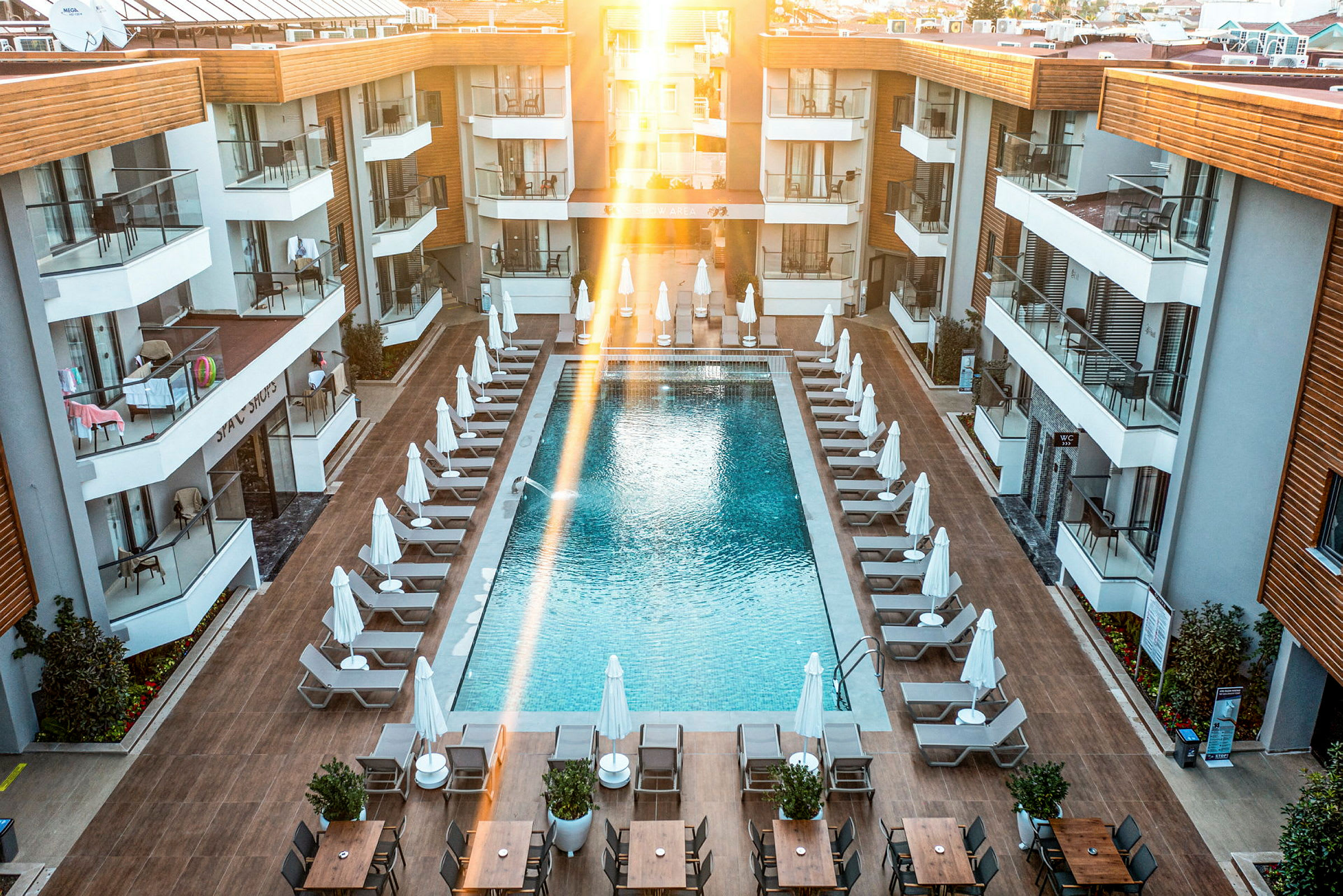 Bilde av et hotellbassengområde med solsenger og parasoller rundt et rektangulært basseng, omgitt av moderne hotellbygninger. (AI-generert tekst)