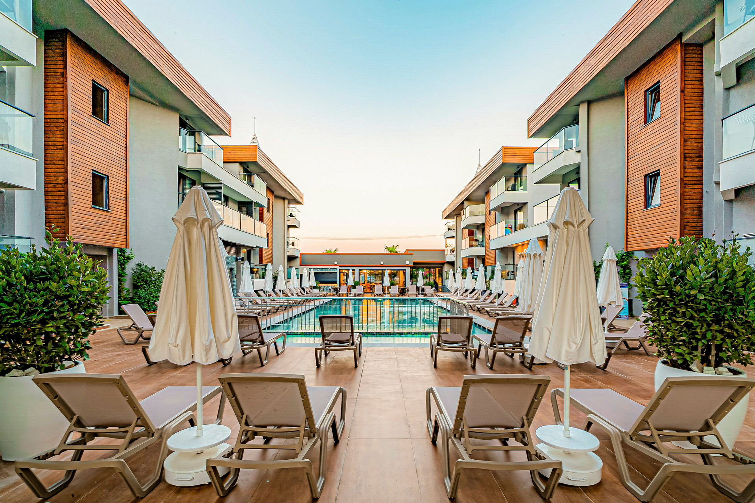 Hotellområde med et basseng og solsenger omgitt av bygninger. (AI-generert tekst)