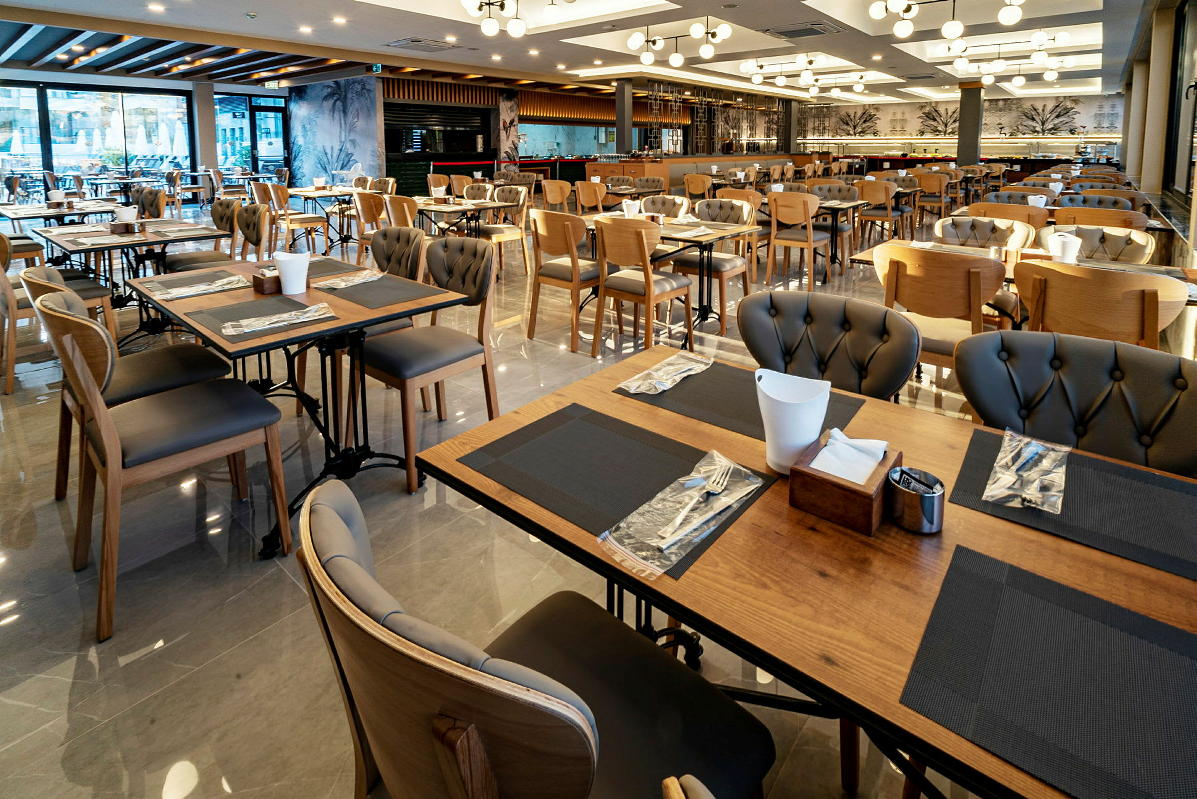 Bilde av en restaurant med mange bord og stoler, elegante borddekorasjoner og moderne belysning. (AI-generert tekst)