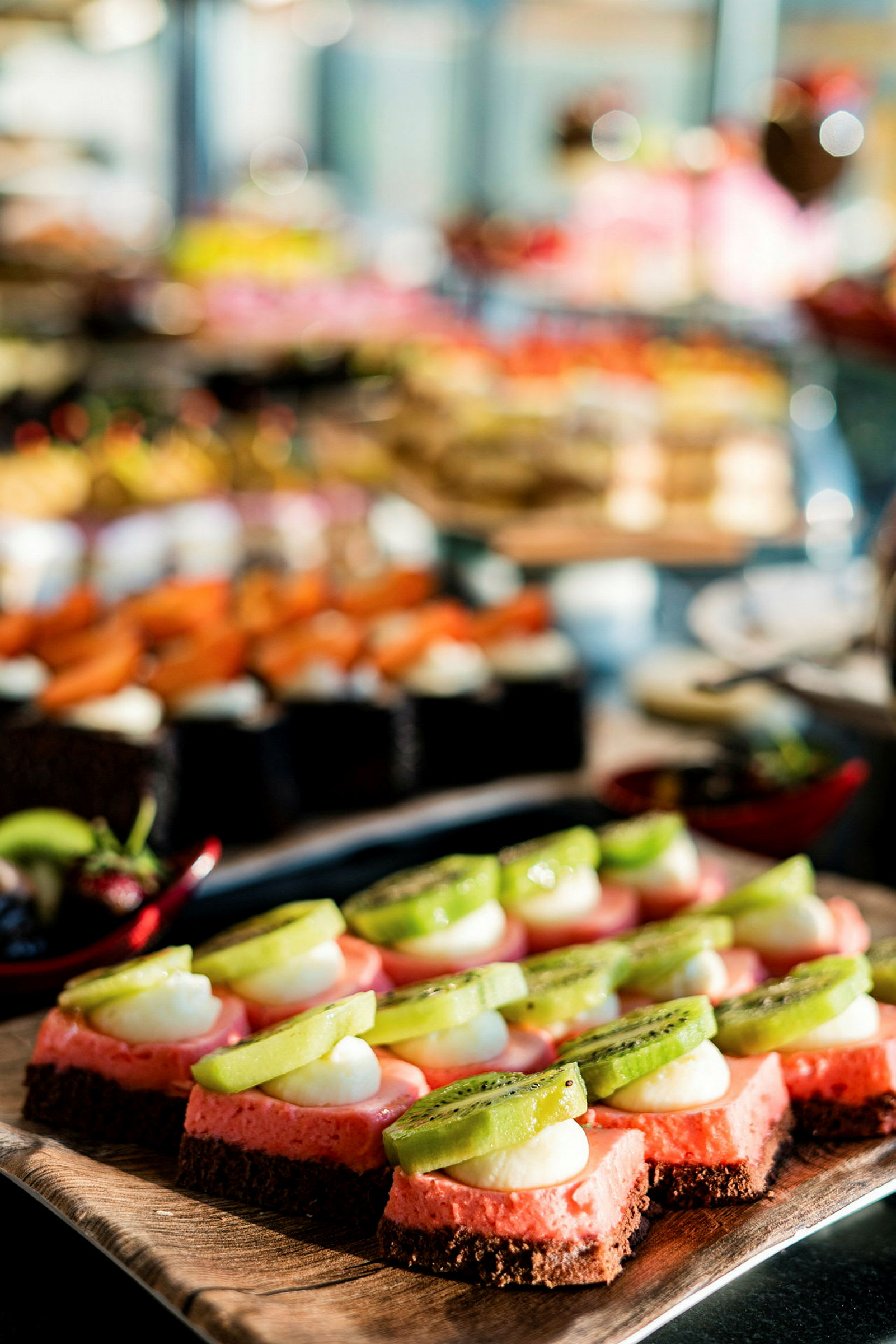 Nærbilde av små dessertbiter toppet med kiwi og krem på en buffet. (AI-generert tekst)