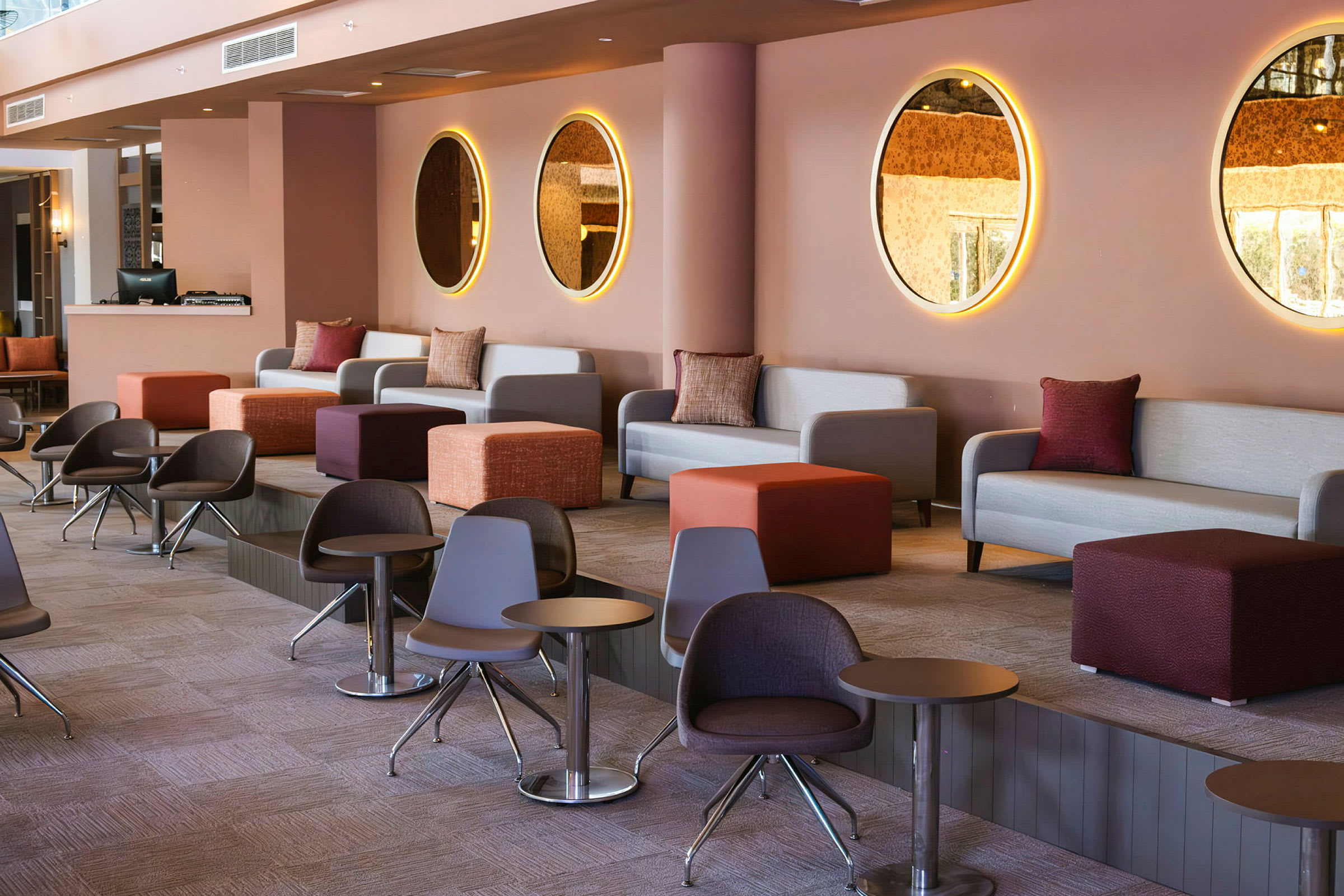 En moderne og fargerik lounge med sofaer, små bord og runde speil på veggen. (AI-generert tekst)