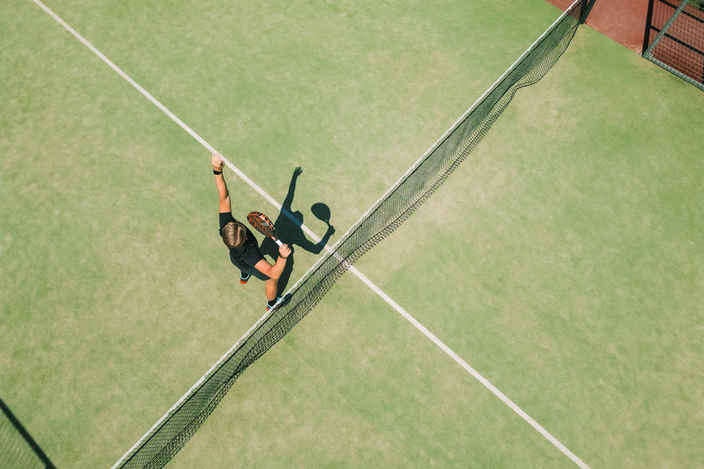 En person spiller tennis på en grønn bane og er i ferd med å slå en ball med en racket. (AI-generert tekst)