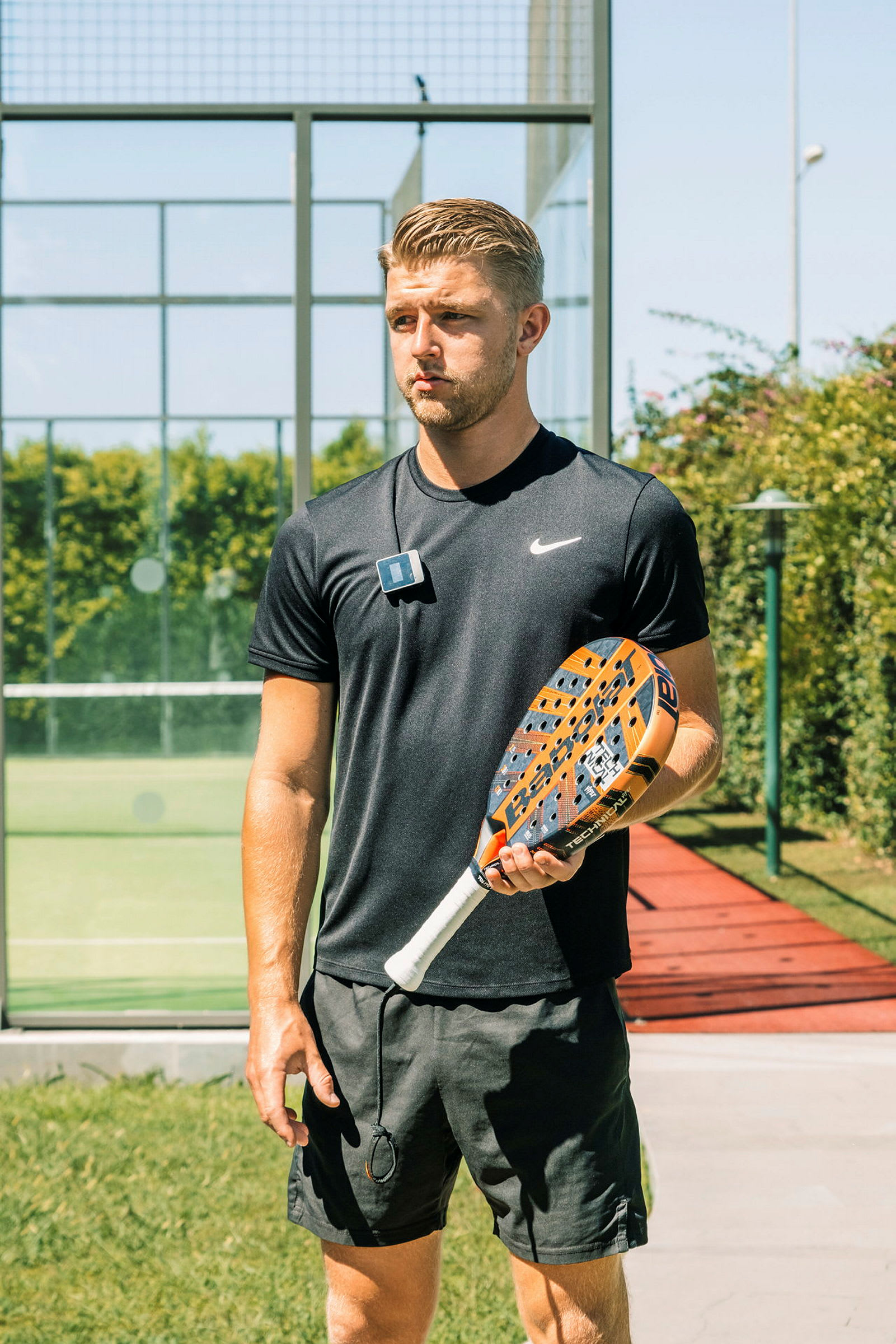 En person holder et padelracket på en utendørs padelbane. (AI-generert tekst)