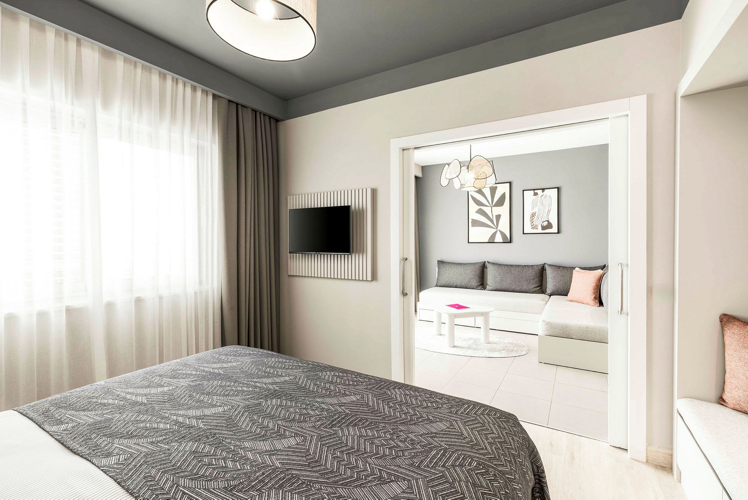 Hotellrom med en seng i forgrunnen, en TV på veggen og en separat sittegruppe med sofa og bord. (AI-generert tekst)