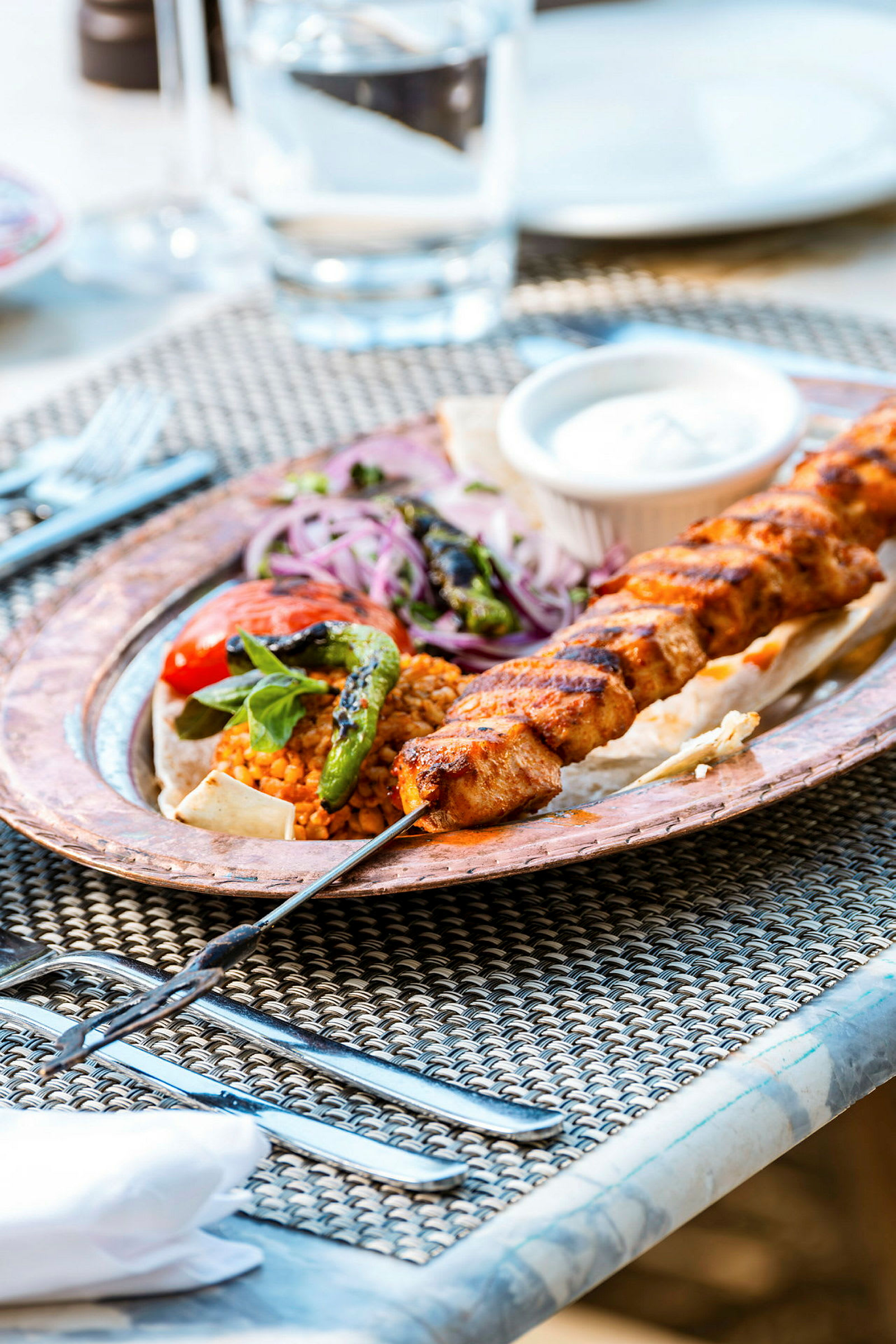 En tallerken med grillspyd, grønnsaker og saus på et bord. (AI-generert tekst)