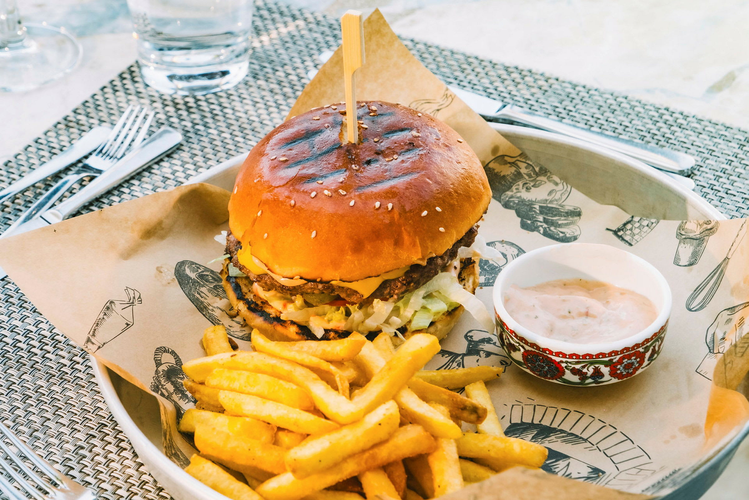 En hamburger servert på en tallerken med pommes frites og en skål saus. (AI-generert tekst)