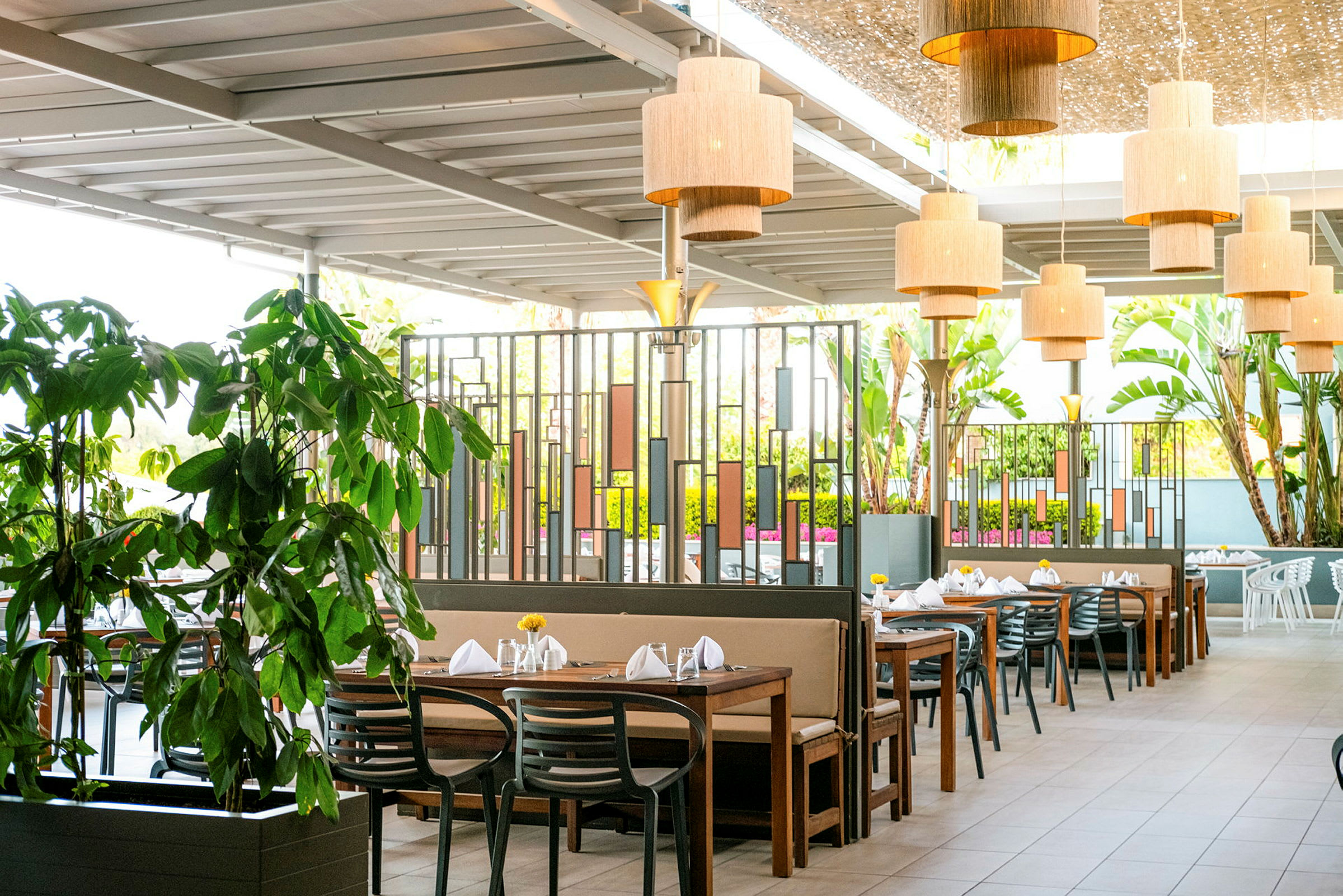 Bilde av en utendørsrestaurant med flere bord, stoler og grøntområder. (AI-generert tekst)