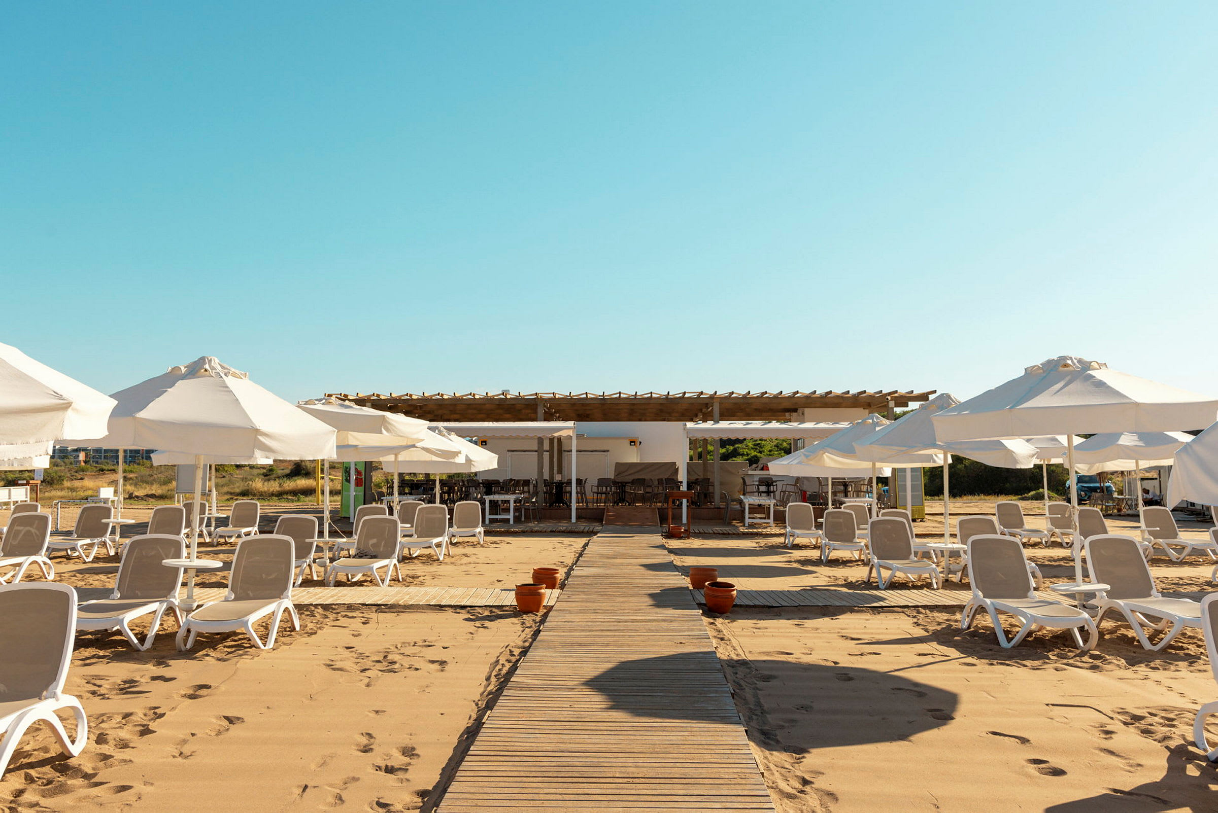 En strand med solsenger og parasoller på sanden, samt en strandbar i bakgrunnen. (AI-generert tekst)