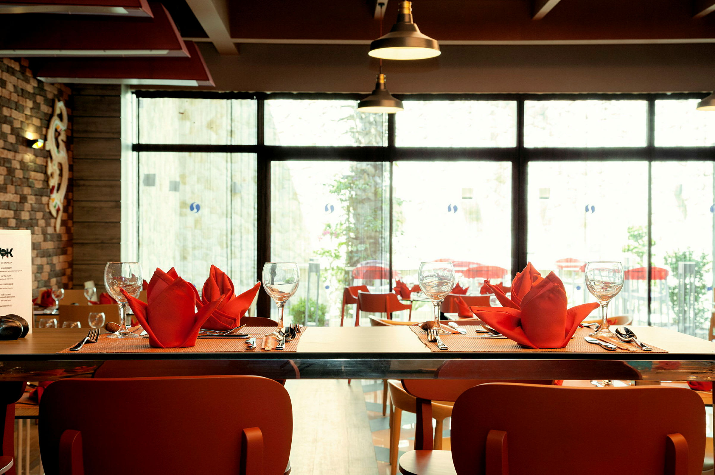 Bord på restaurant med røde servietter, glass og bestikk oppdekket. (AI-generert tekst)