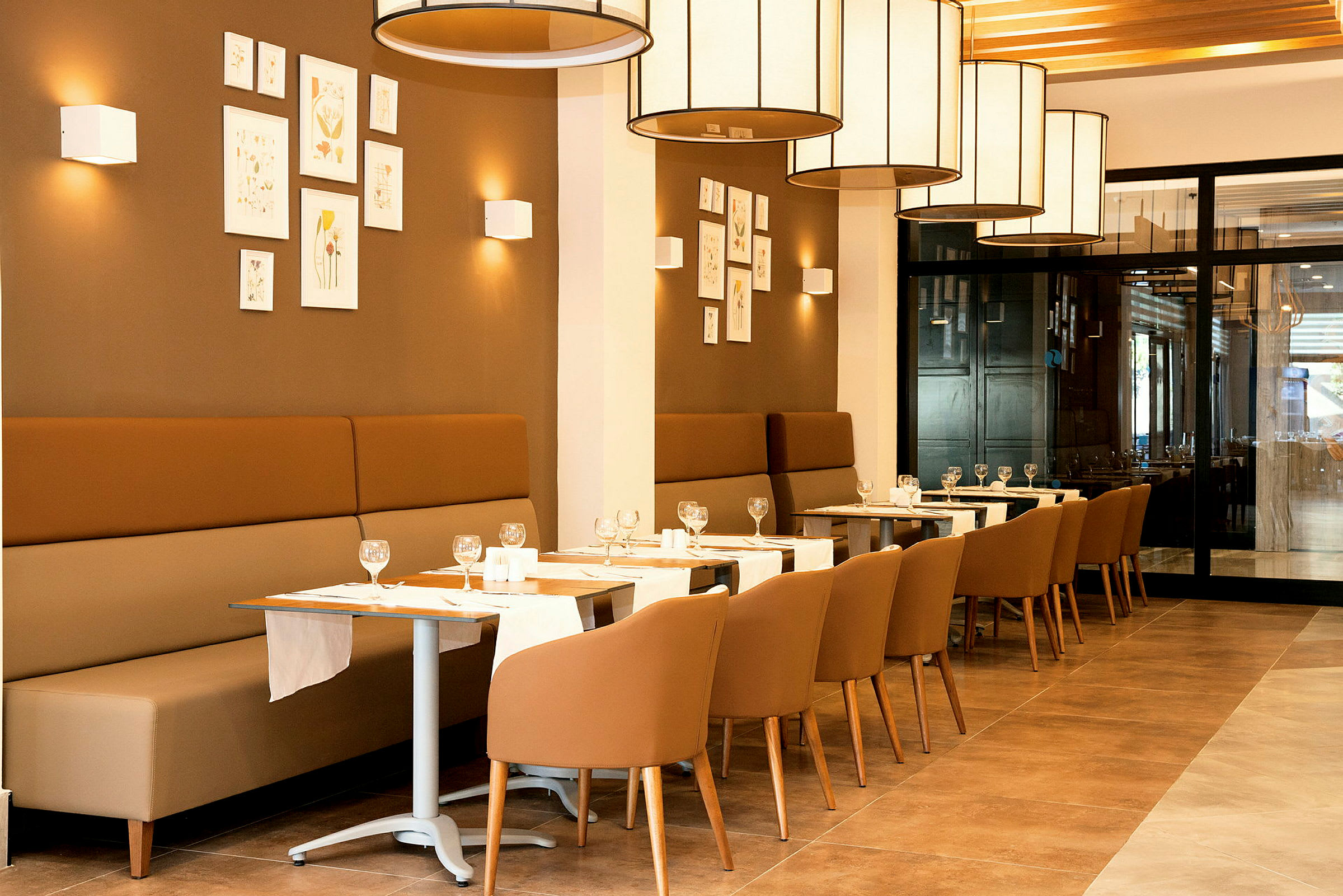 En restaurant med sitteplasser og bord dekket med glass og servietter. (AI-generert tekst)