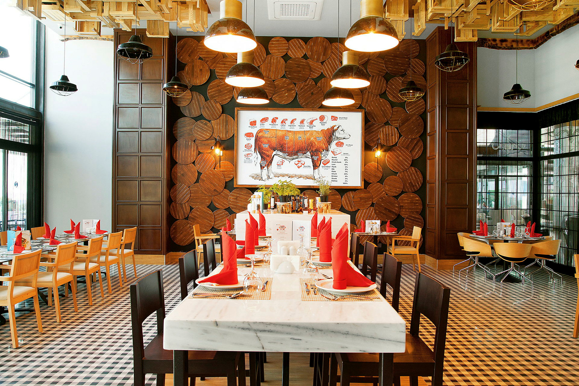 Interiøret til en restaurant med spisebord, røde servietter og en illustrasjon av storfekjøtt på veggen. (AI-generert tekst)