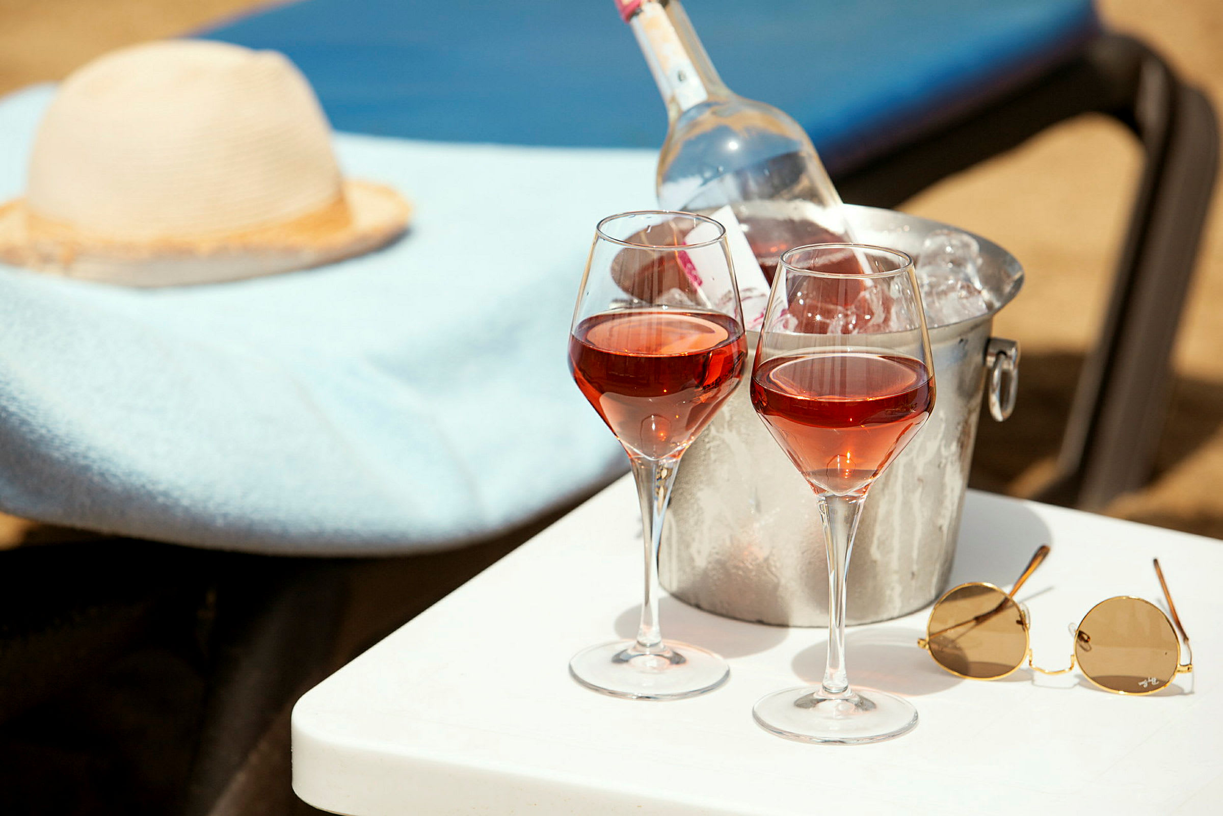 To glass rosévin og en bøtte med vinkjøler på et bord ved en solseng. (AI-generert tekst)