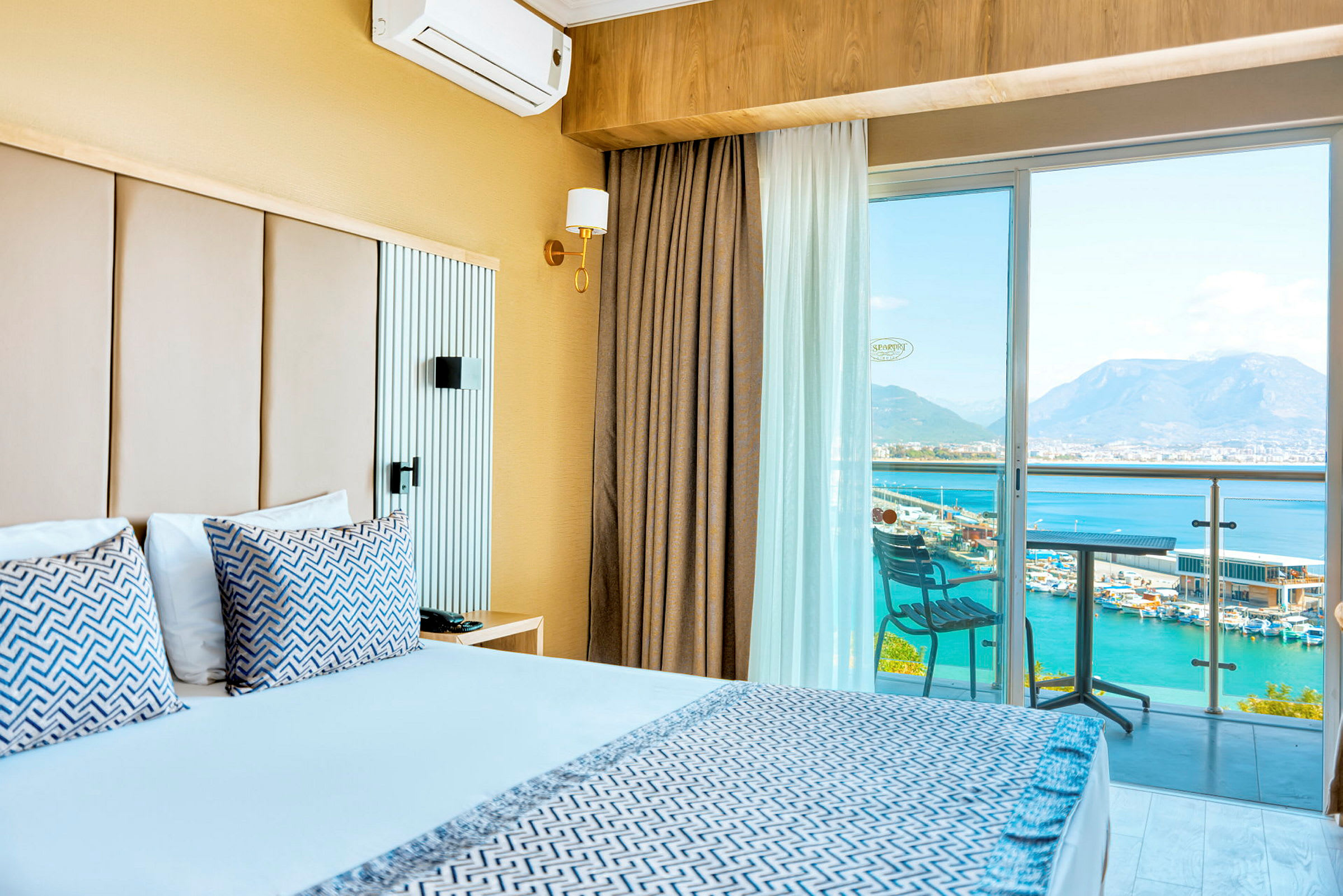Hotellrom med dobbeltseng, balkong med utsikt over havet og fjellene. (AI-generert tekst)