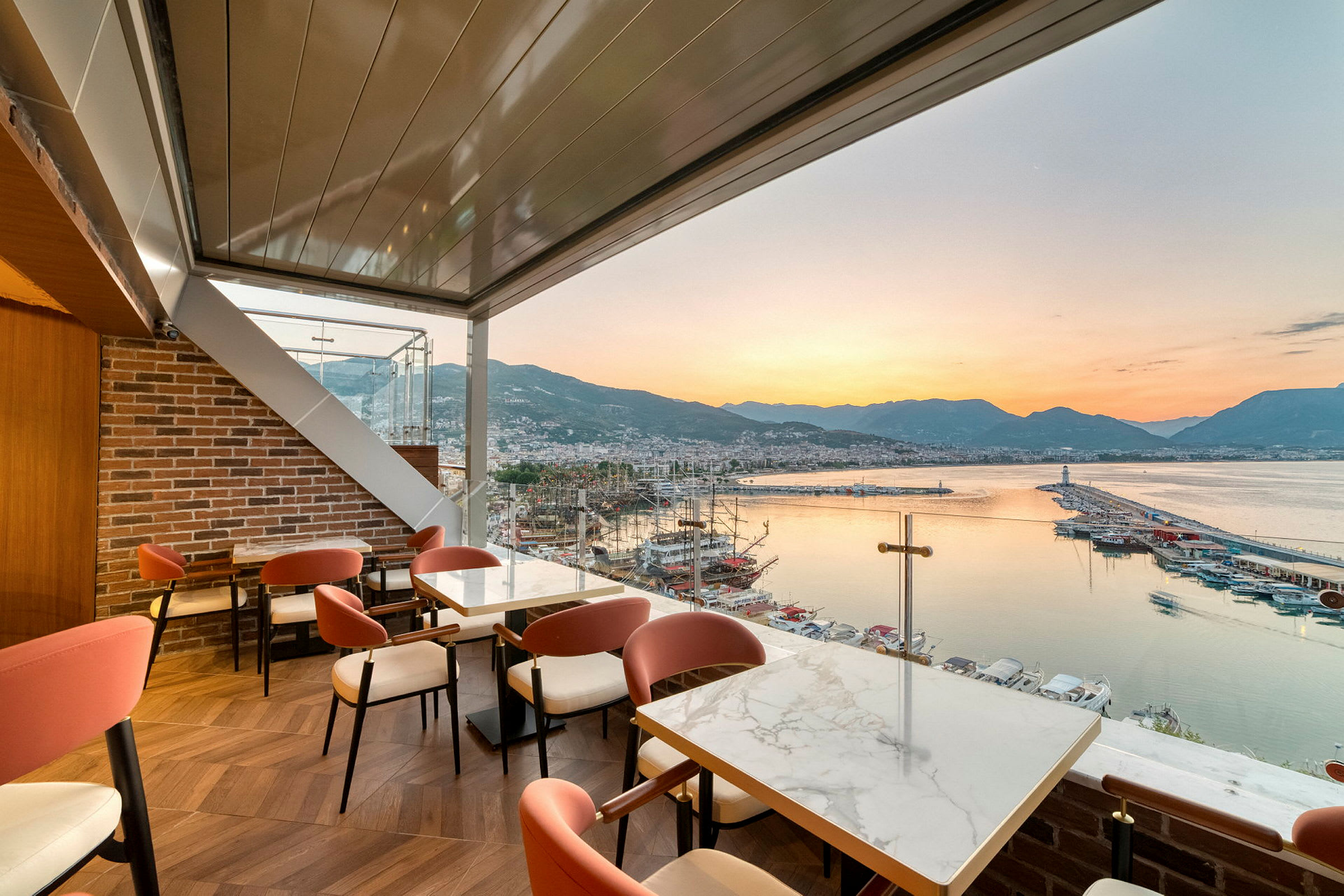 Restaurant med utsikt over en havn, sjøen og fjellene ved solnedgang. (AI-generert tekst)