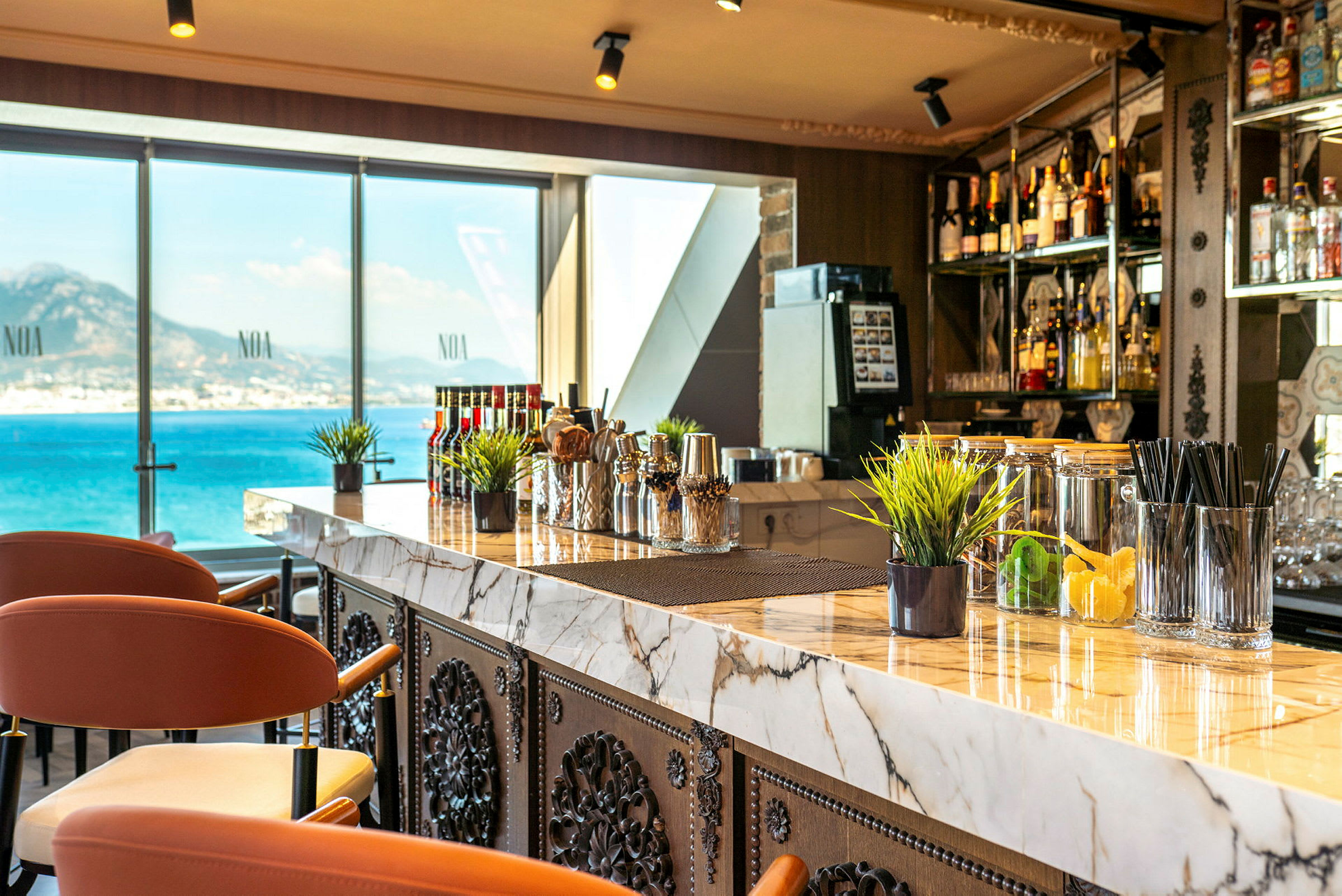 En moderne bar med marmorbord og stoler samt utsikt over havet gjennom store vinduer. (AI-generert tekst)