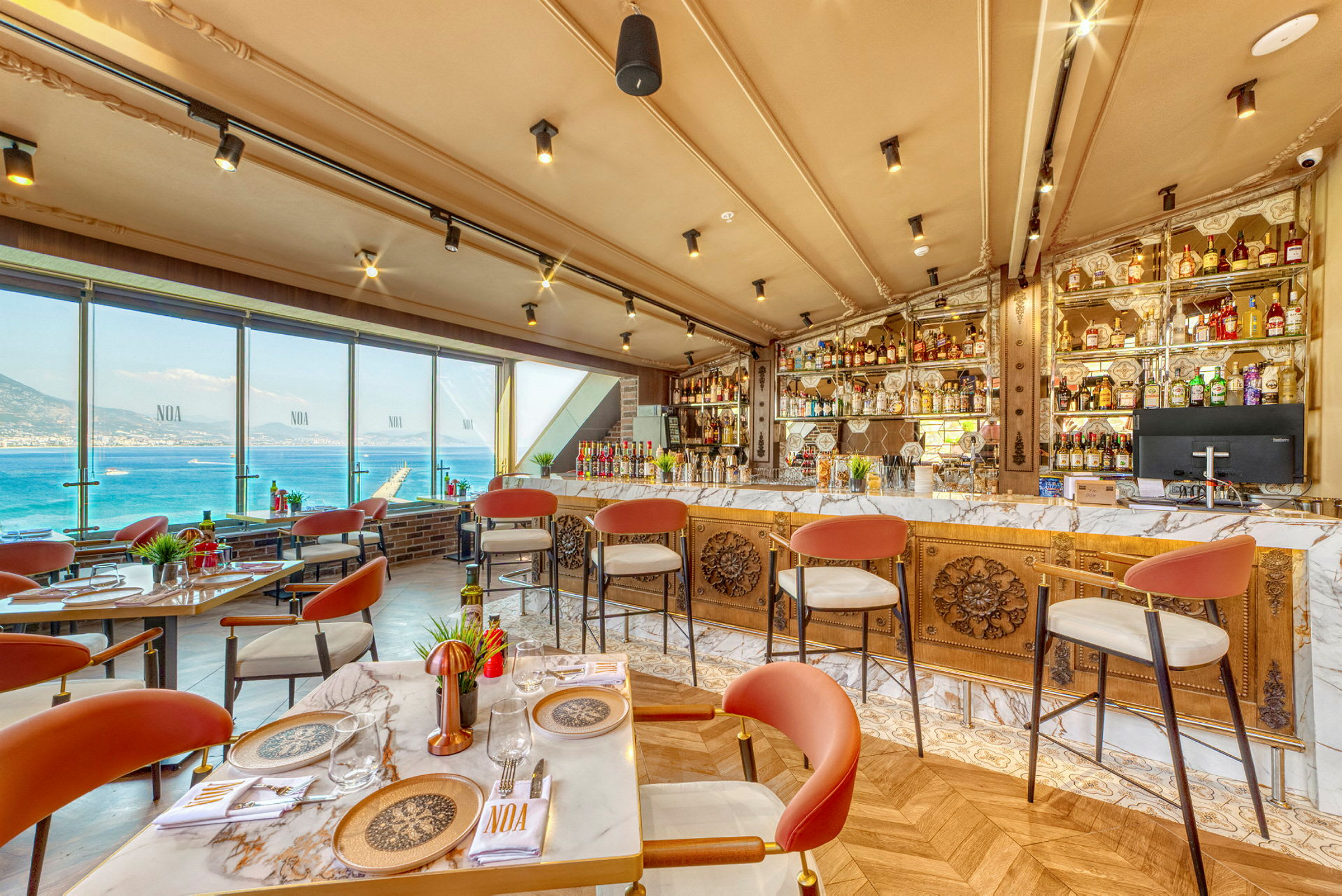 Restaurant med utsikt over havet, bord og stoler, samt en velutstyrt bar. (AI-generert tekst)