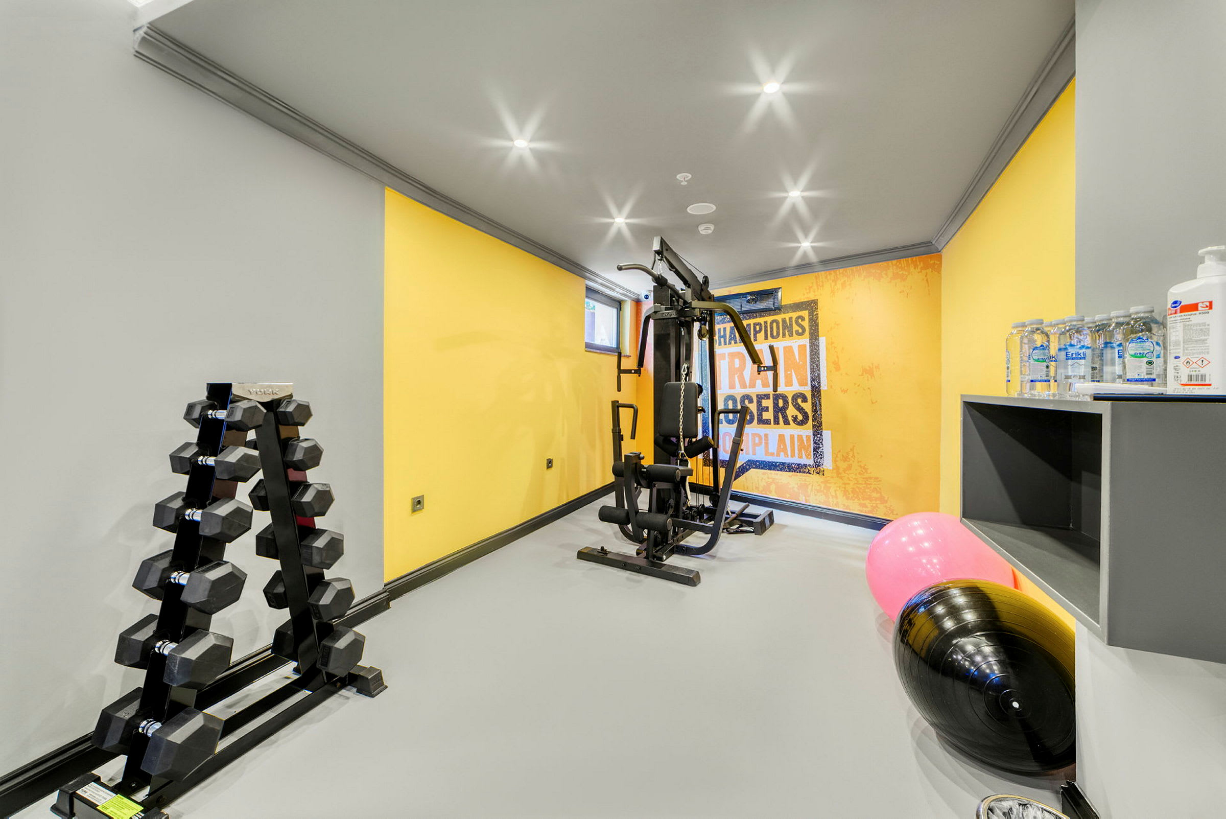 Et gym med treningsutstyr, hantler, en plakat på veggen og vannflasker. (AI-generert tekst)