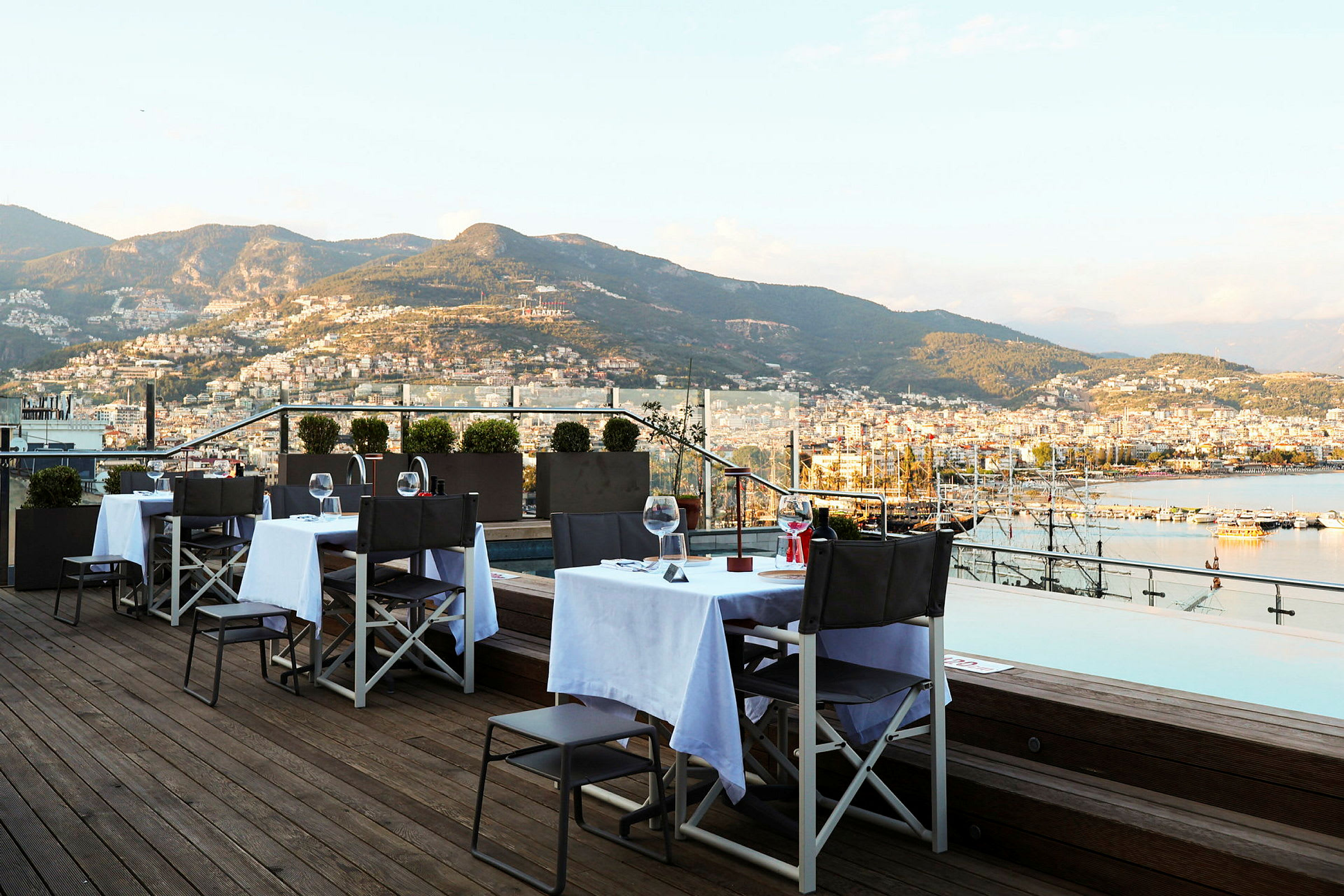 Restaurantbord på en terrasse med utsikt over fjell og hav. (AI-generert tekst)